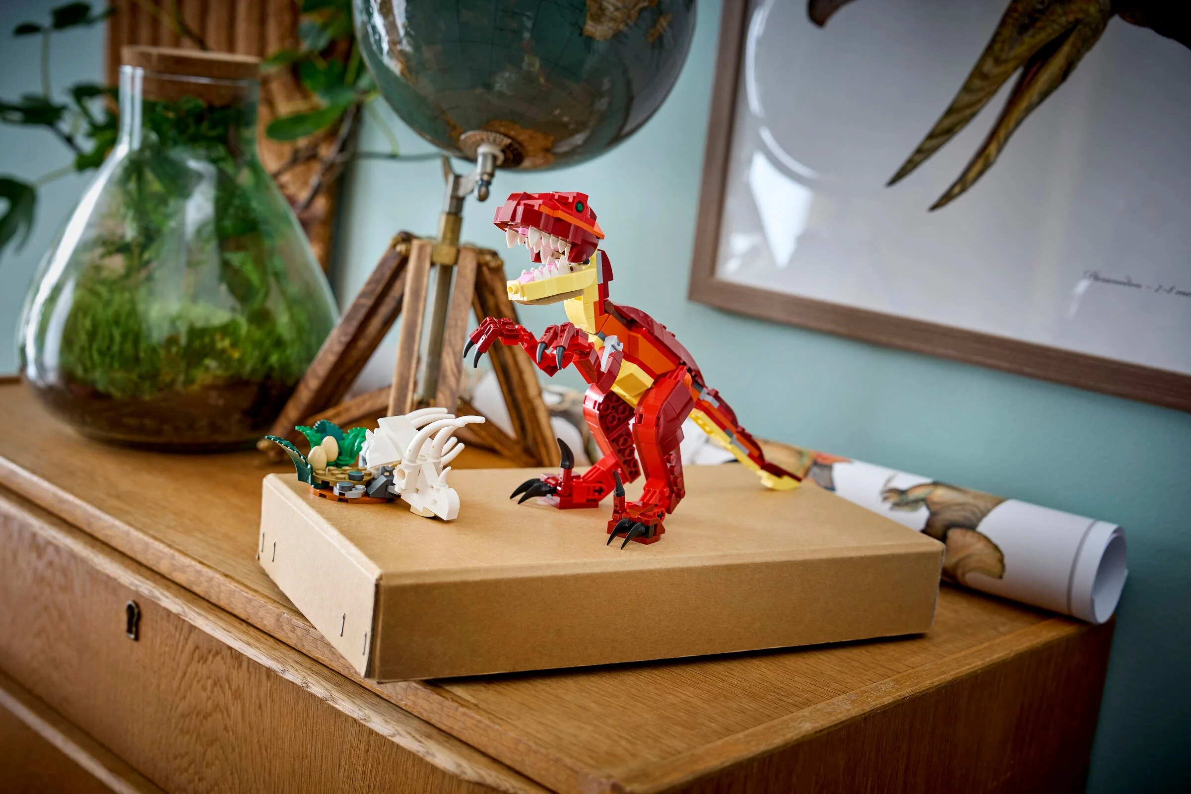 Dinozaurul roșu LEGO 31379 stând amenințător lângă un craniu de triceratops pe o cutie maro.