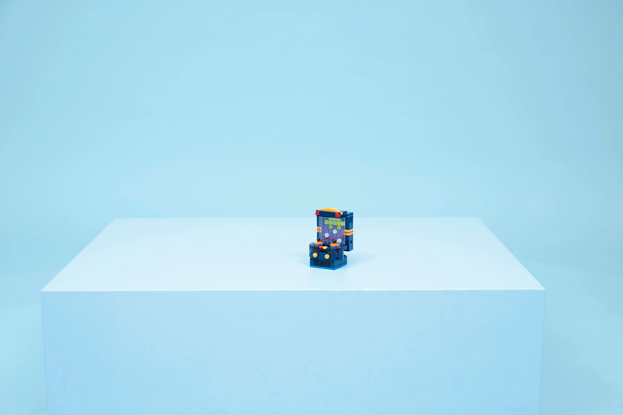 O consolă retro LEGO, albastră și portocalie, pe un cub albastru, fundal simplu.