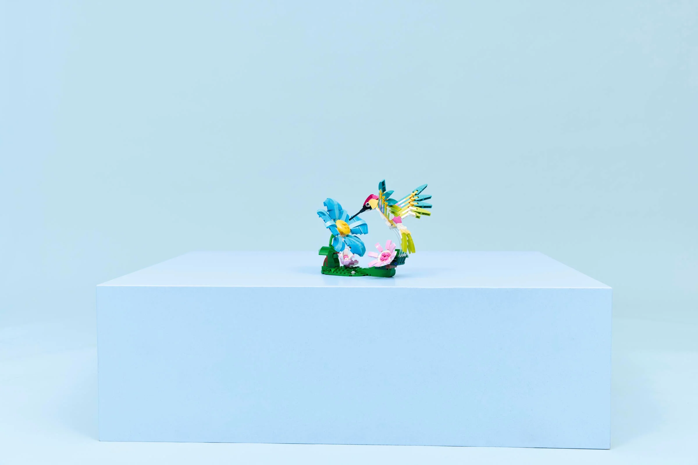 Un colibri colorat LEGO Creator, ce vizitează o floare albastră și una roz.