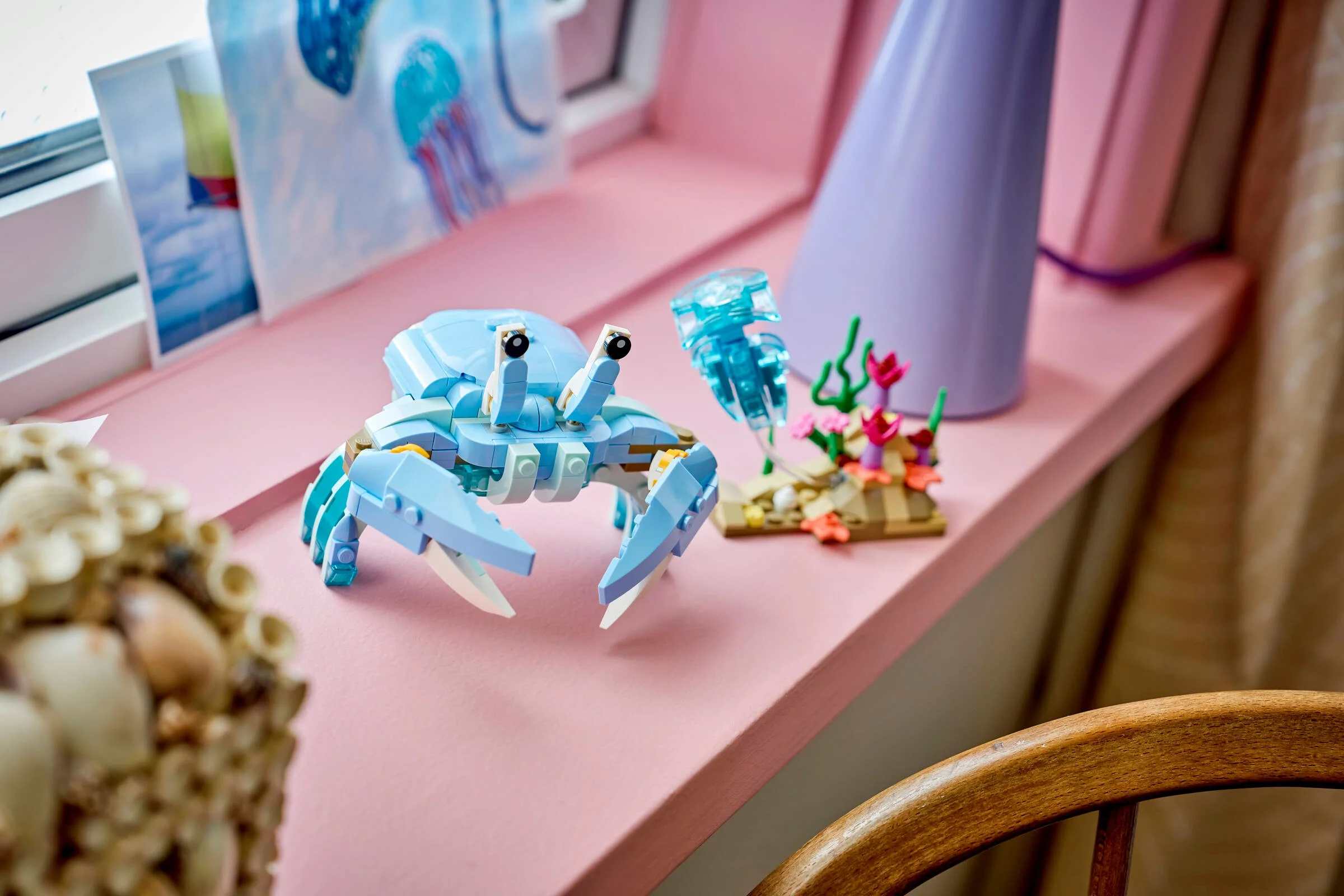 Imagine cu un crab LEGO albastru, o meduză și coral pe un pervaz roz. Detalii frumoase!