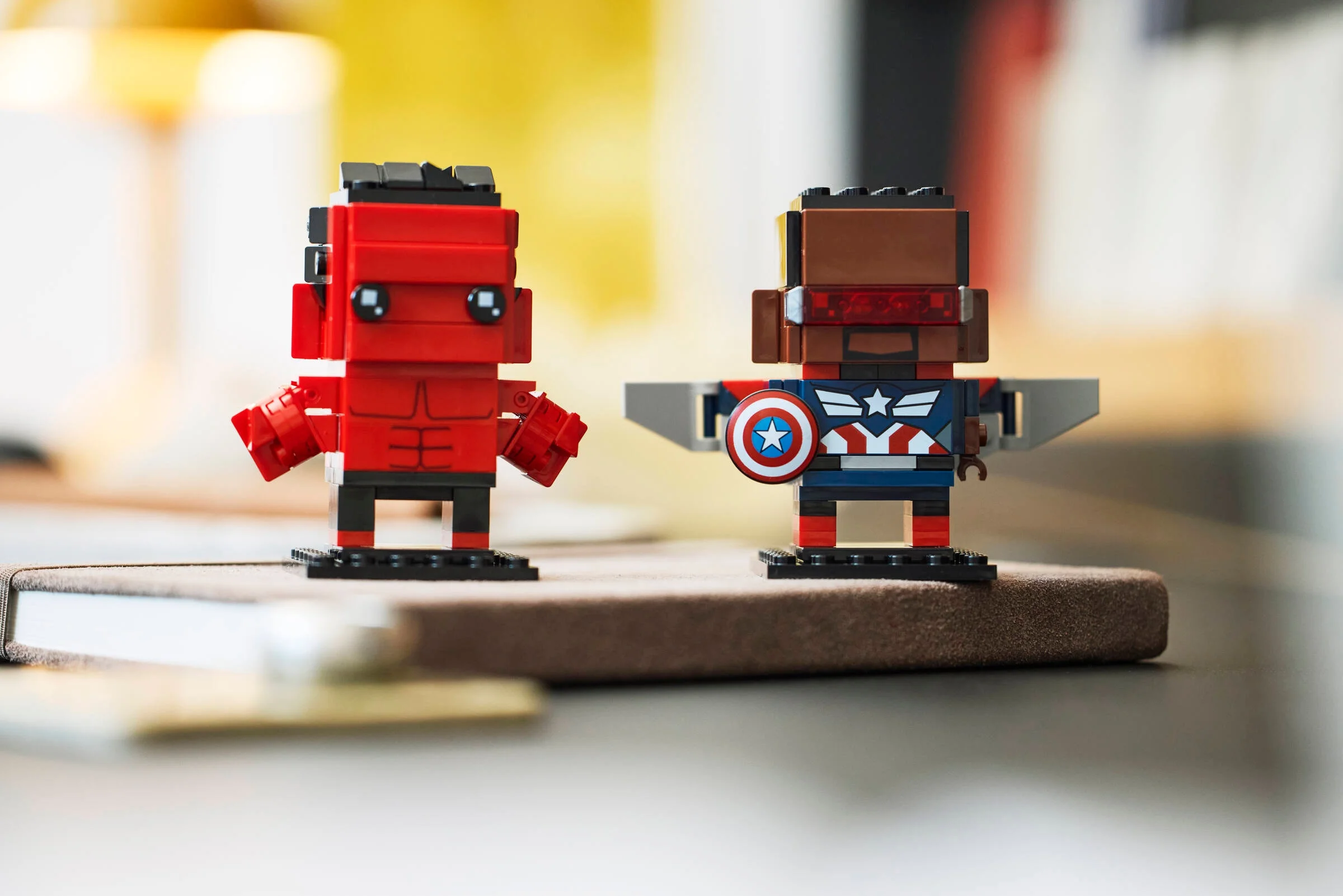 Imagine cu figurinele Captain America și Red Hulk BrickHeadz, stând pe o suprafață maro.