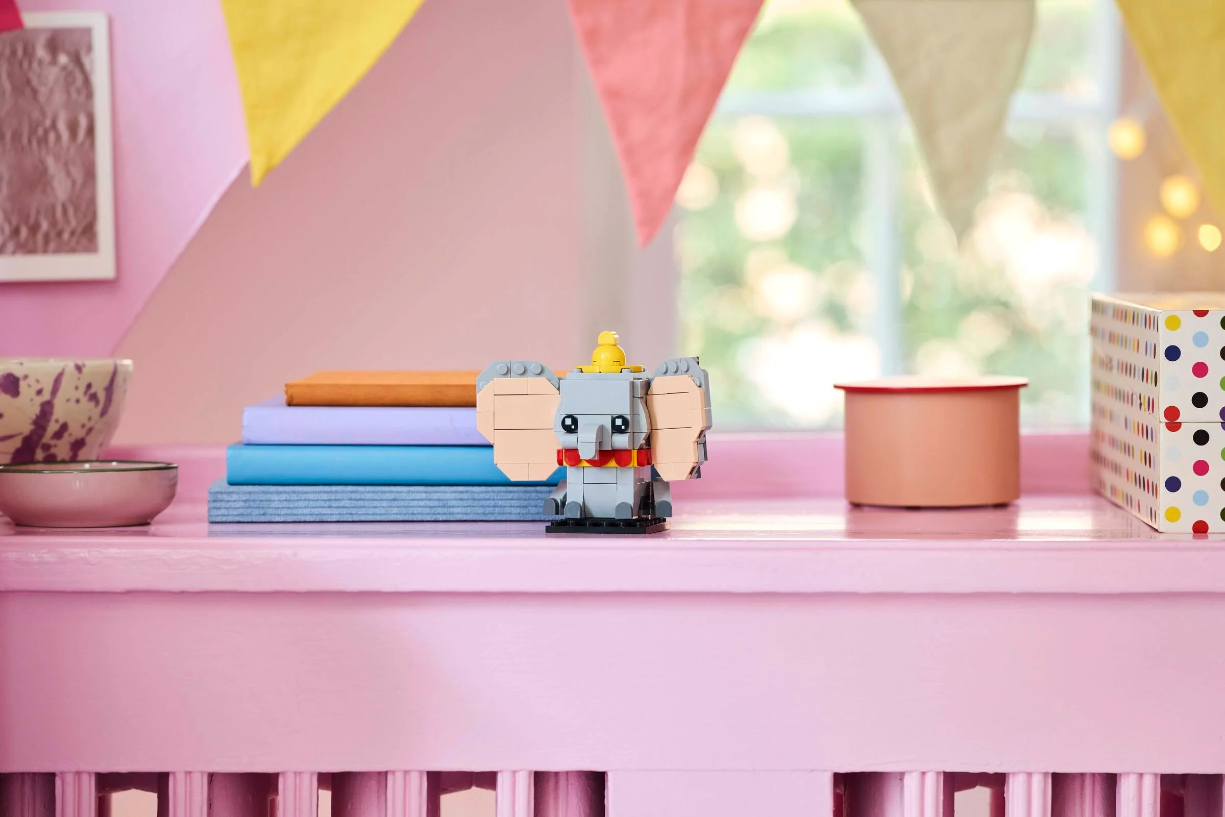 Dumbo BrickHeadz LEGO pe un raft roz, într-o cameră decorată festiv.