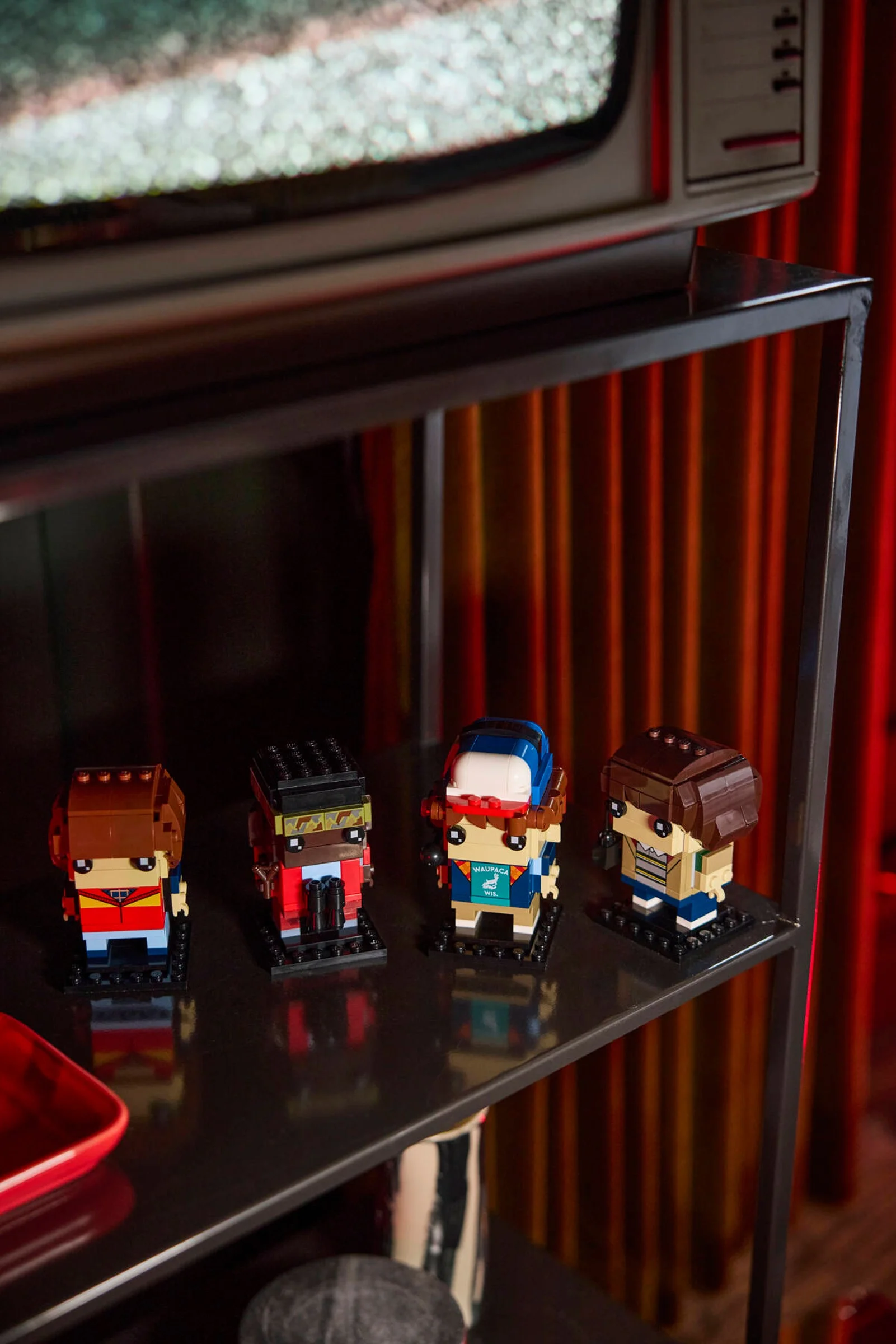 Imagine cu figurinele BrickHeadz Mike, Dustin, Lucas și Will pe un raft, cu fundal tematic.