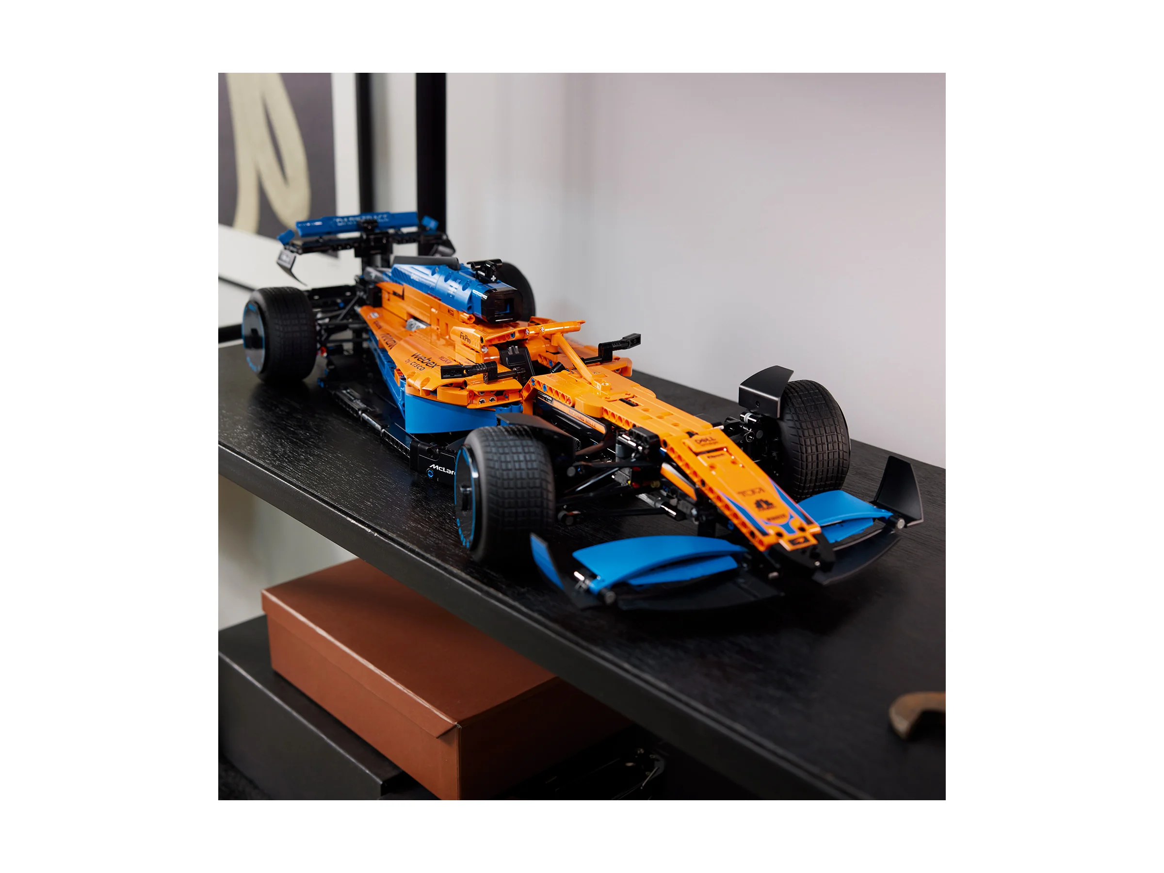 Mașină McLaren Formula 1 Technic, portocalie și albastră, pe un raft. Model detaliat.