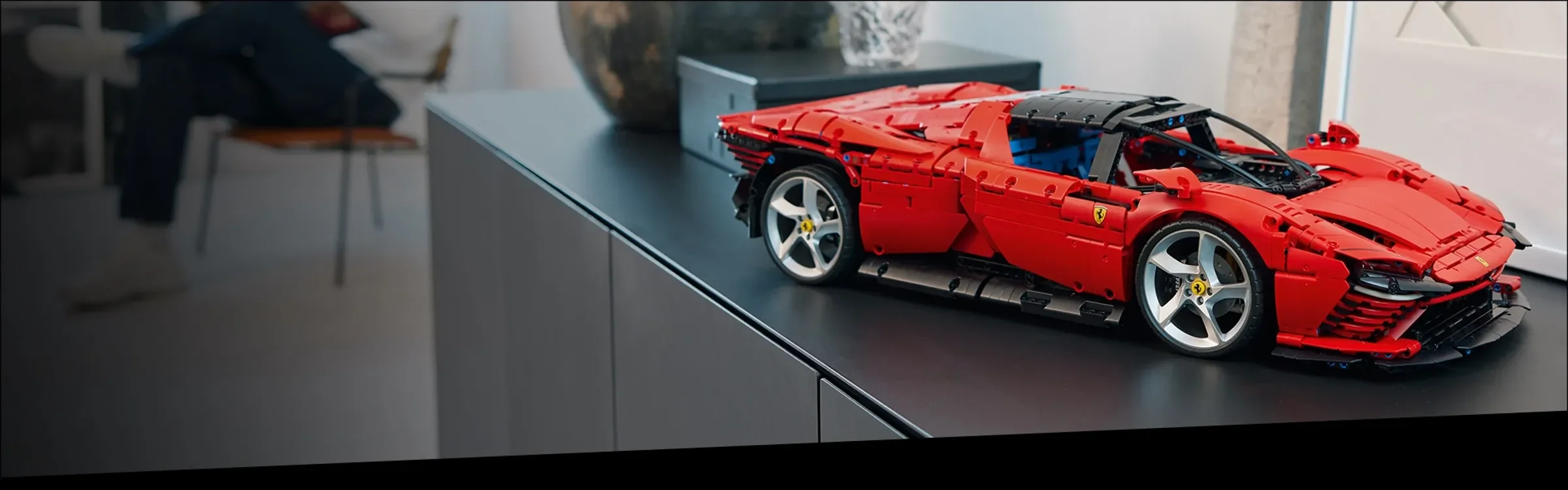 Ferrari Daytona SP3 roșu, o mașină sport LEGO Technic, expusă pe un bufet modern.