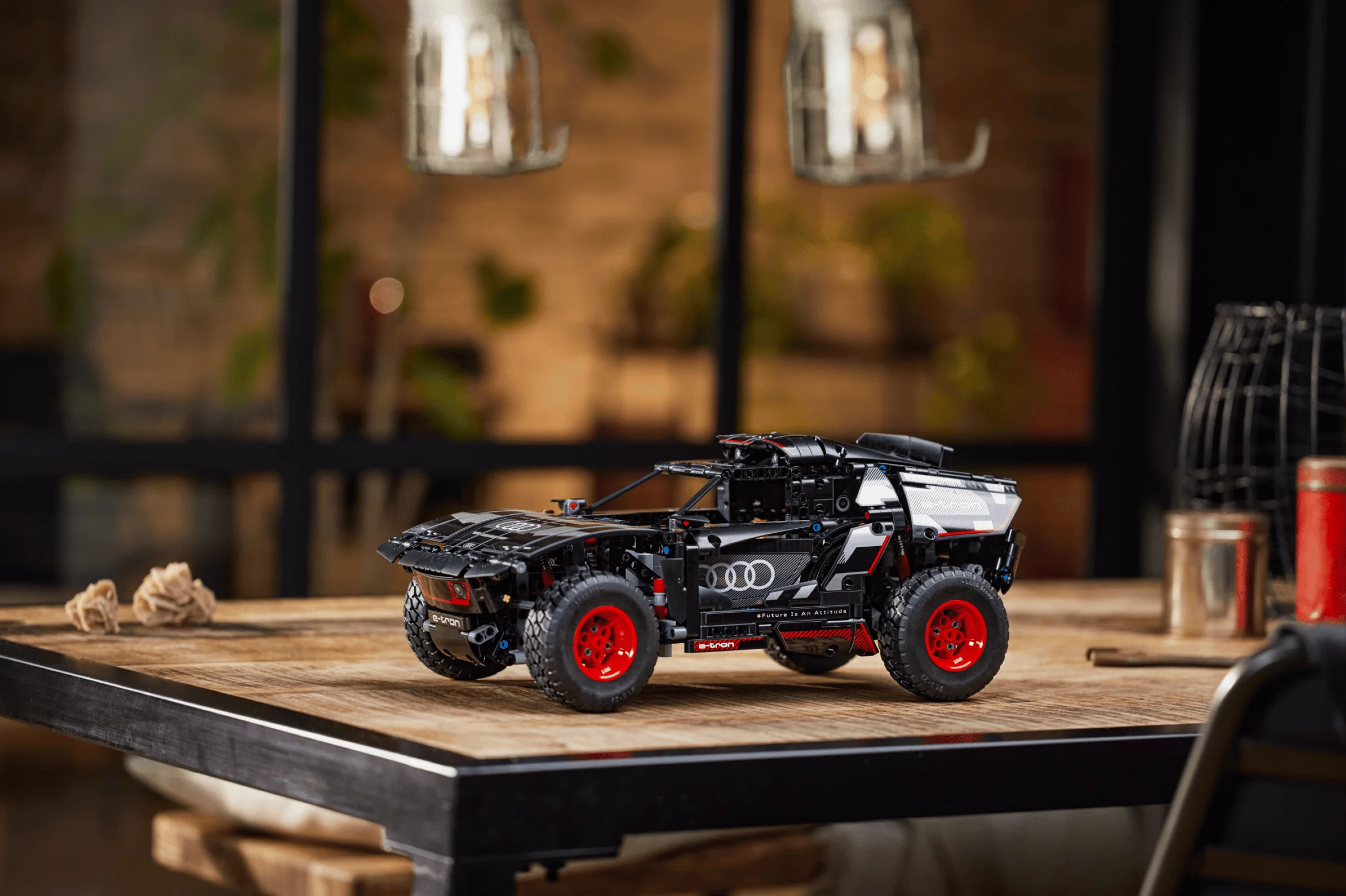 Imagine cu modelul Audi RS Q e-tron din LEGO Technic, negru cu roți roșii, pe o masă din lemn.
