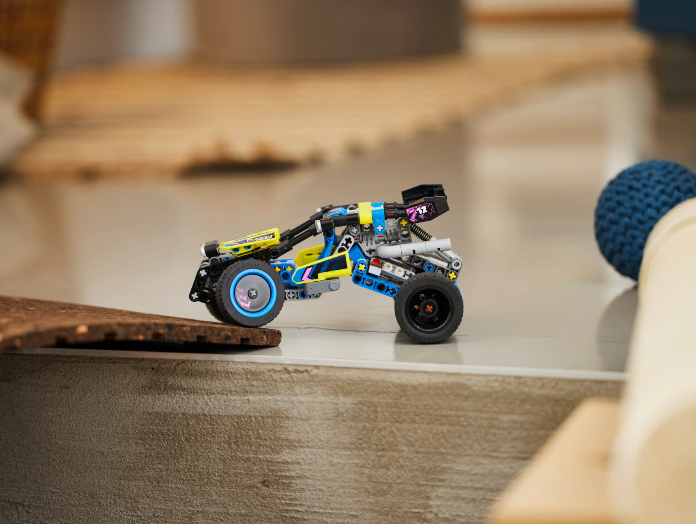 Buggy-ul off-road LEGO Technic galben, albastru și negru pe o rampă mică de lemn.