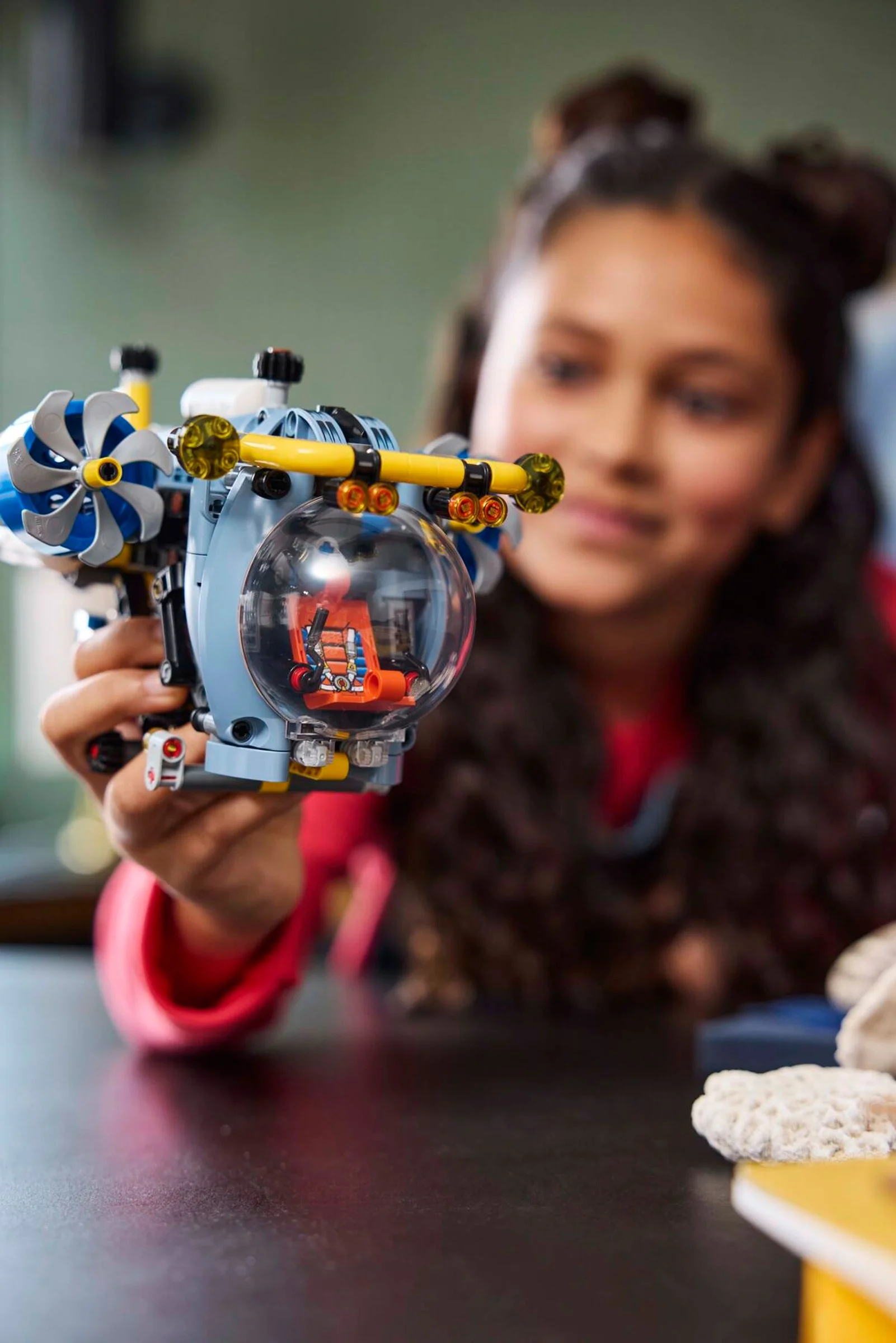 O fată ține submarinul LEGO 42201. Se vede cabina cu scaunul. E lumină și focus bun.