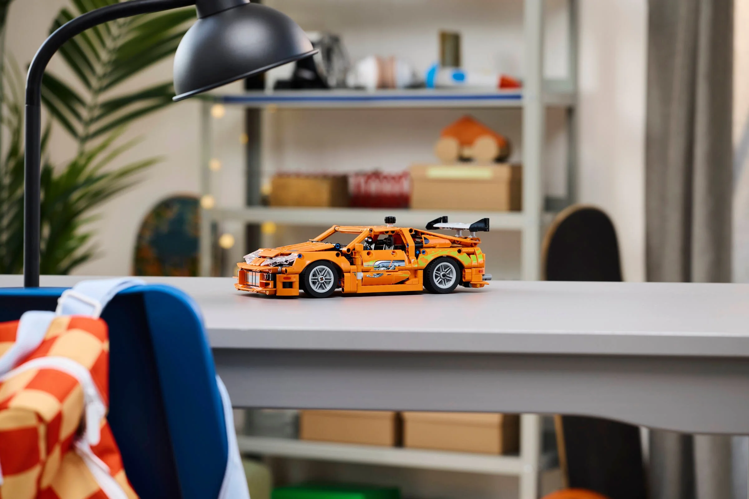 Toyota Supra MK4 portocalie, modelul LEGO Technic, pe o masă într-o cameră.