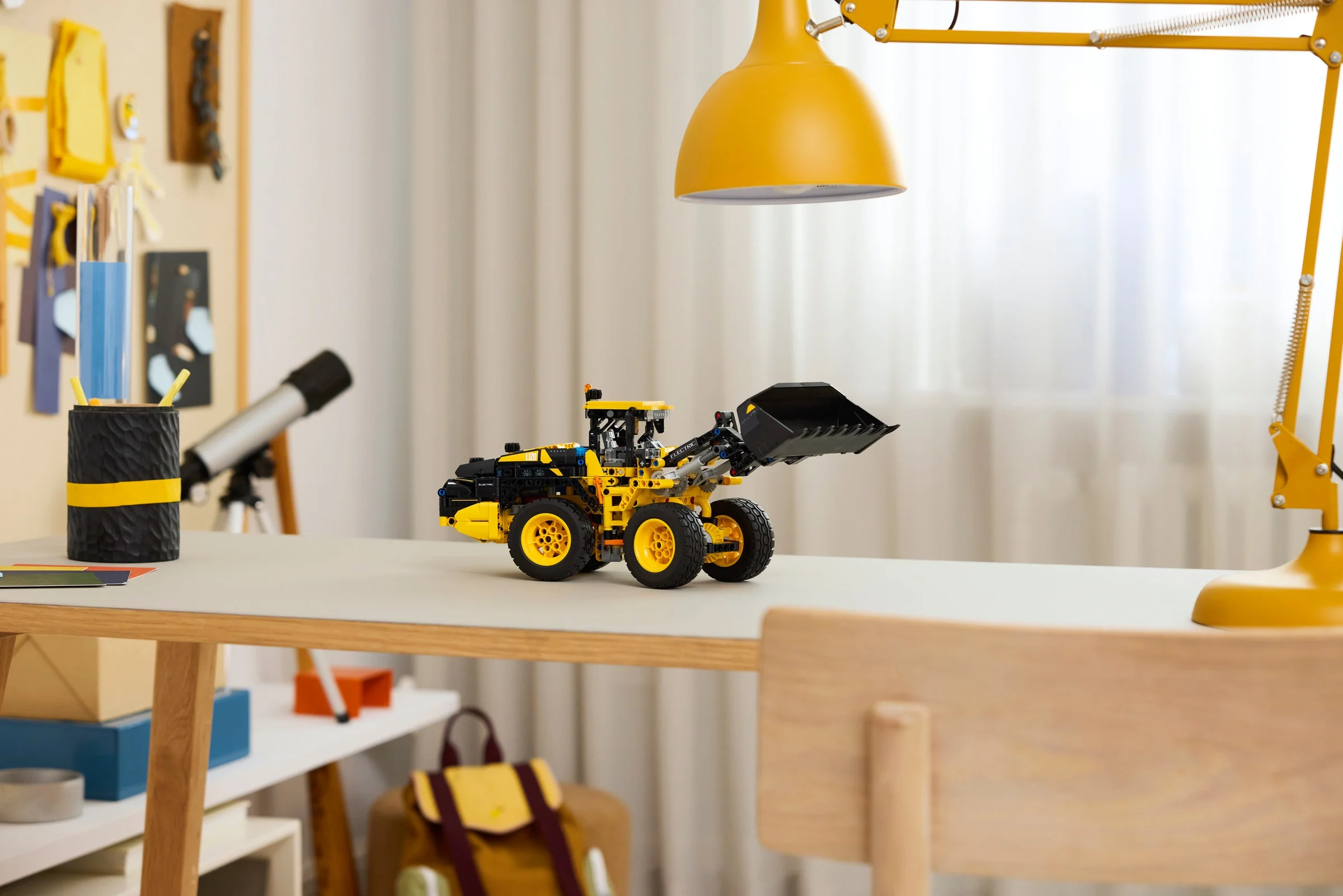 Modelul LEGO Volvo L120, galben și negru, pe o masă luminoasă, cu cupa ridicată.