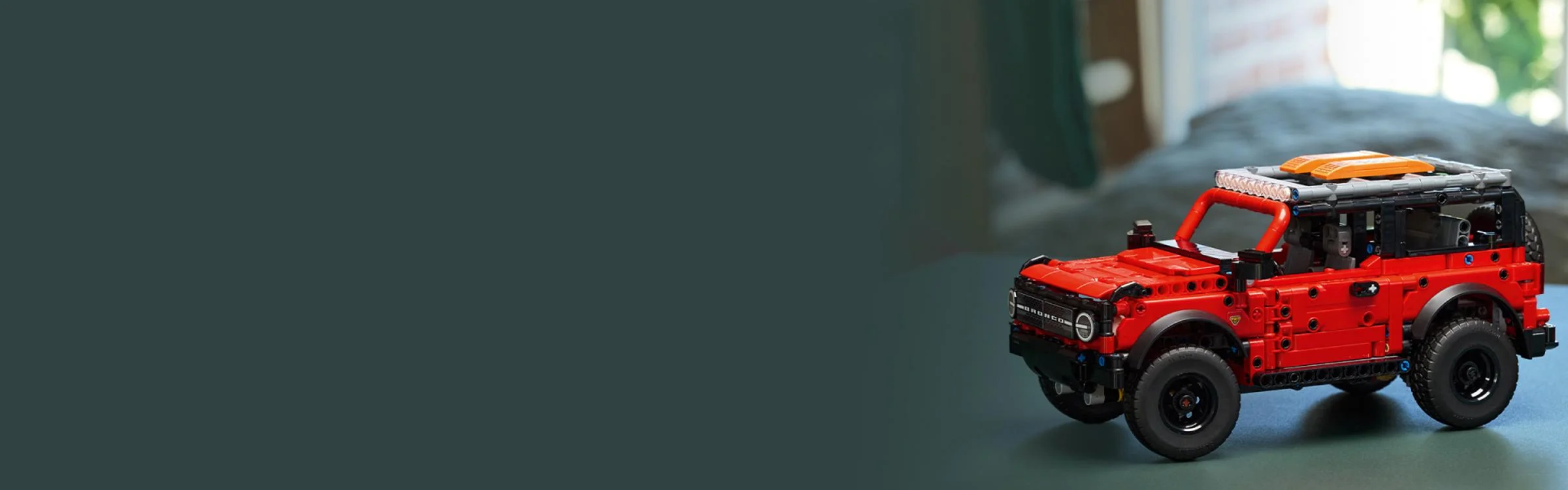 Ford Bronco SUV roșu, model LEGO Technic, expus pe un fundal verde-gri.