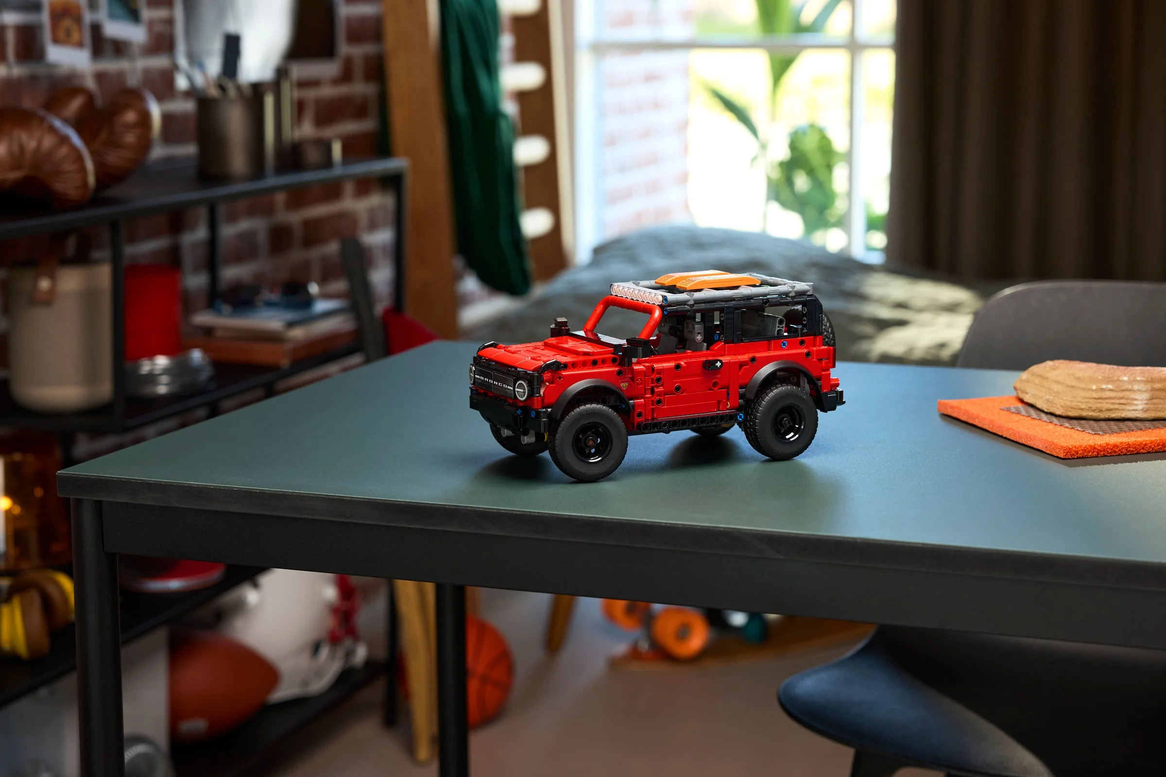 Modelul finalizat Ford Bronco LEGO Technic 42213, prezentat pe o masă, într-un cadru ambiant. Vizualizare din față.