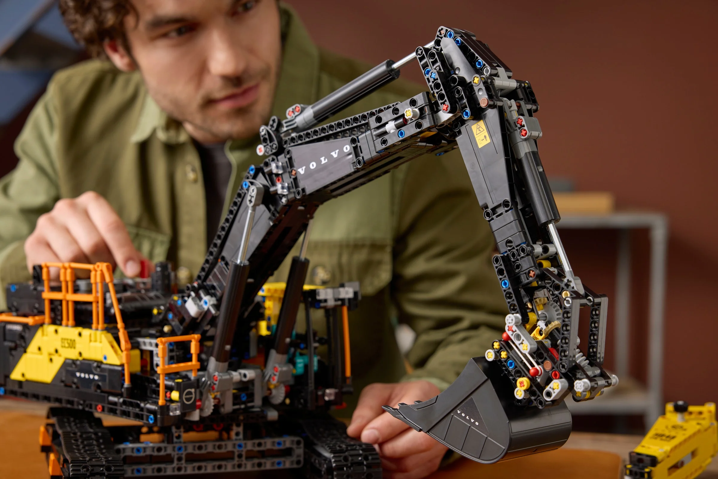 Modelul Volvo EC500 Hybrid Excavator LEGO Technic, detaliu braț excavator, cu o persoană interacționând.