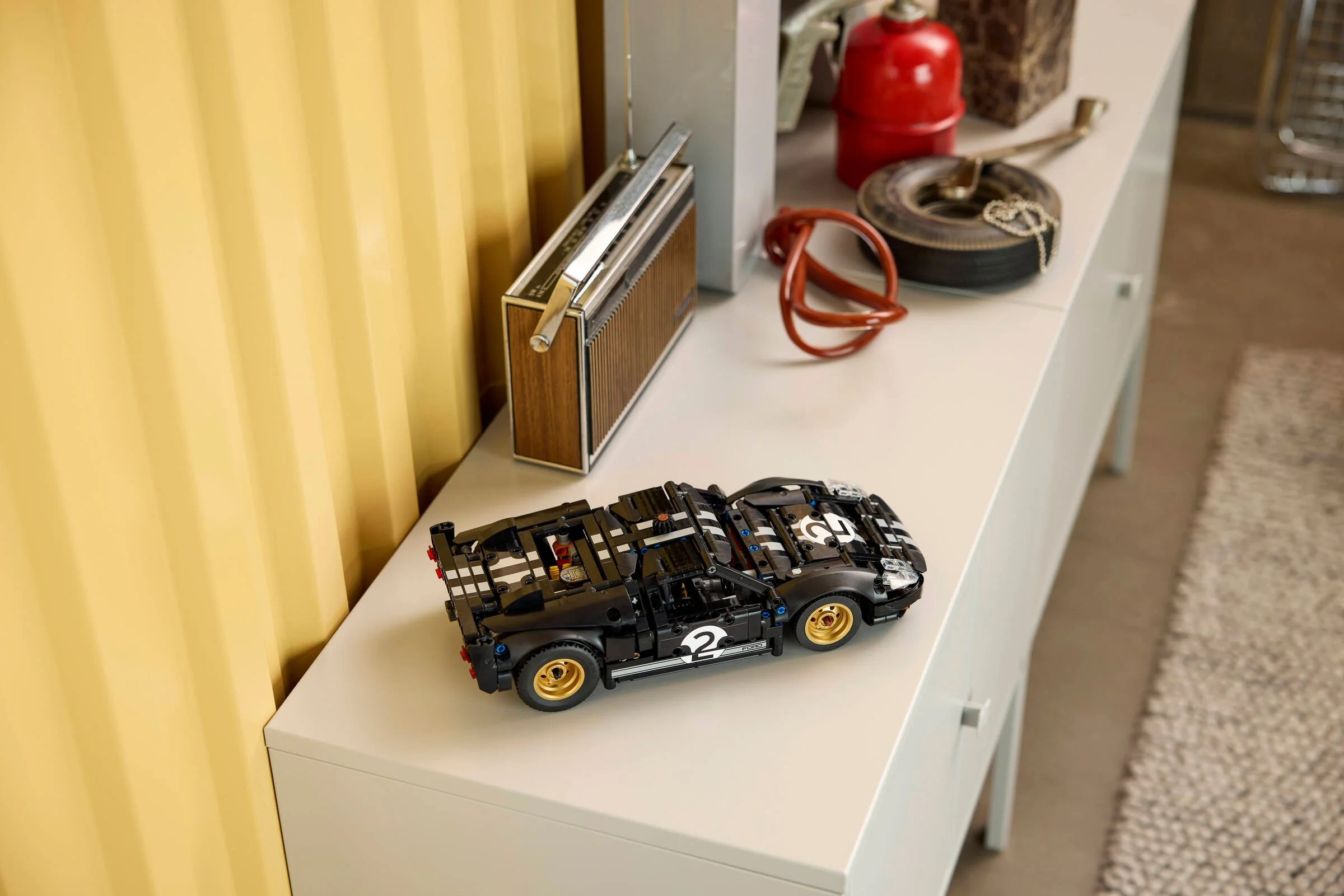 Modelul Ford GT40 MKII negru, expus pe o comodă albă. Detaliile tehnice sunt vizibile.
