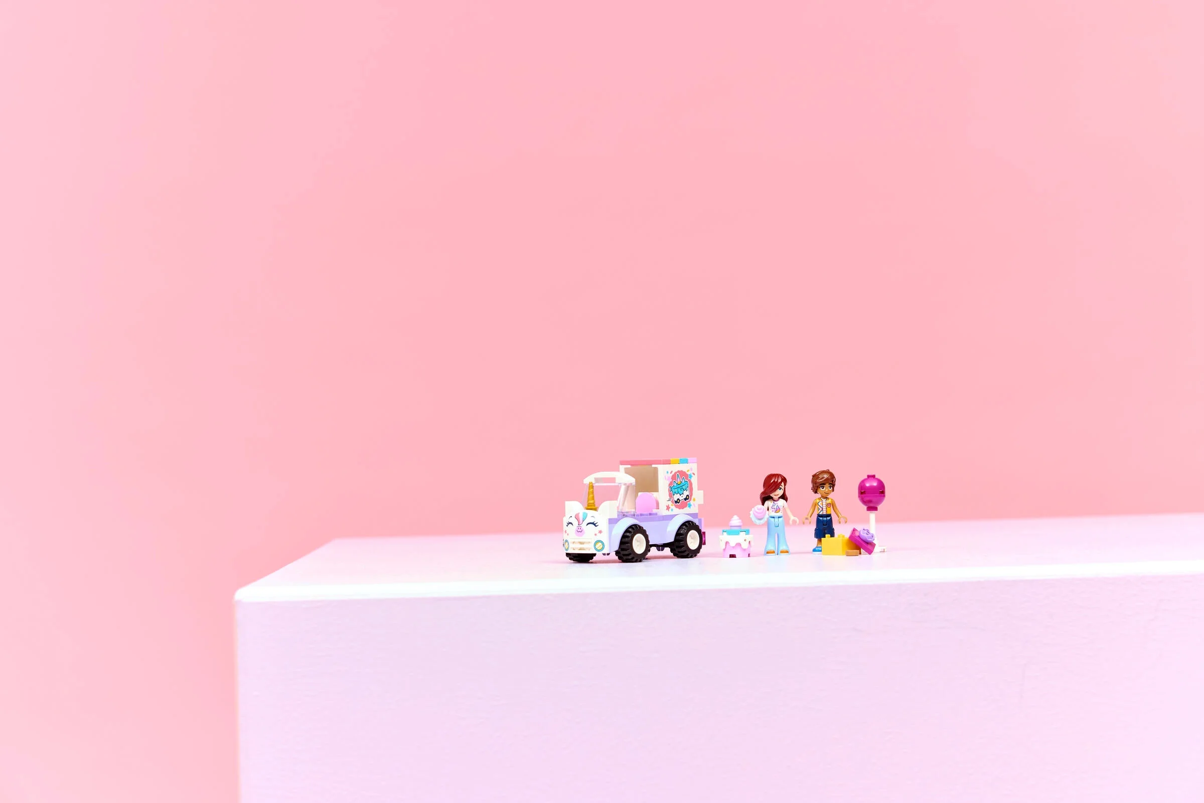 Mașină de livrare prăjituri unicorn LEGO Friends, cu minifigurine și accesorii, pe fundal roz.