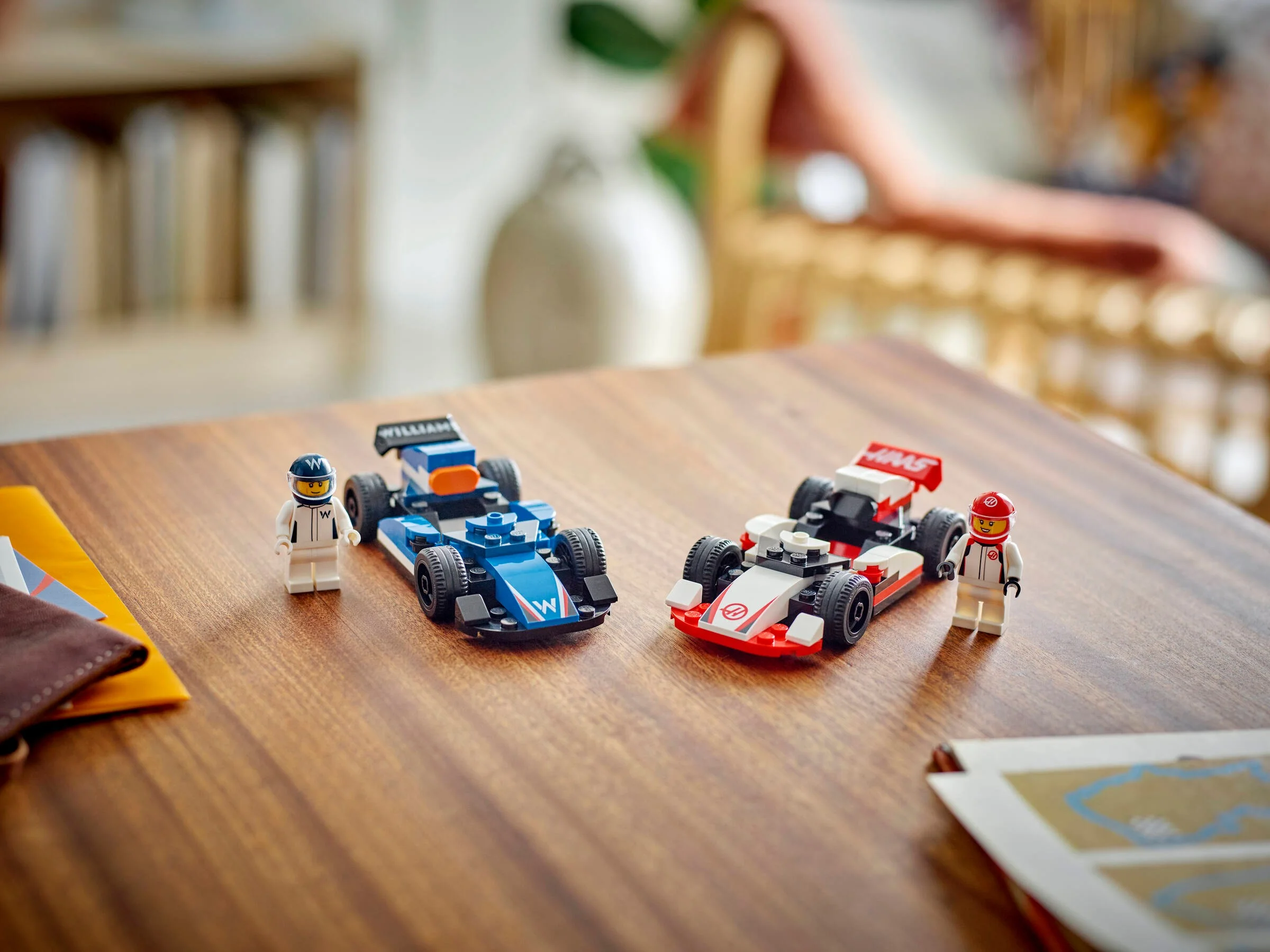 Două mașini de curse F1 LEGO (Williams și Haas) și minifigurinele piloților, pe o masă de lemn.