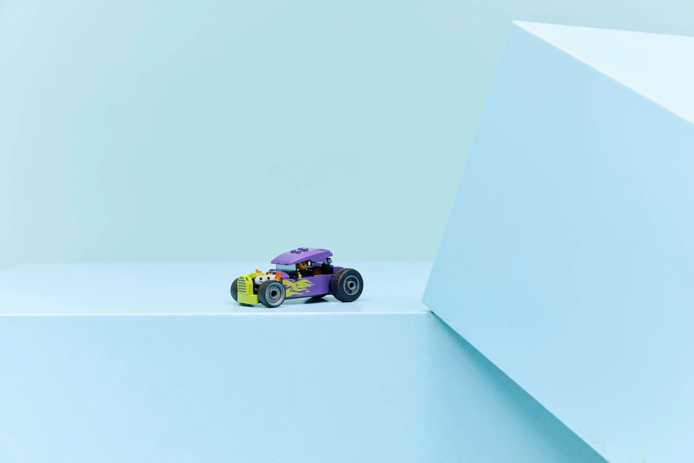 Imagine cu un hot rod LEGO violet și verde, pe un fundal albastru pastel. Modelul e complet asamblat.