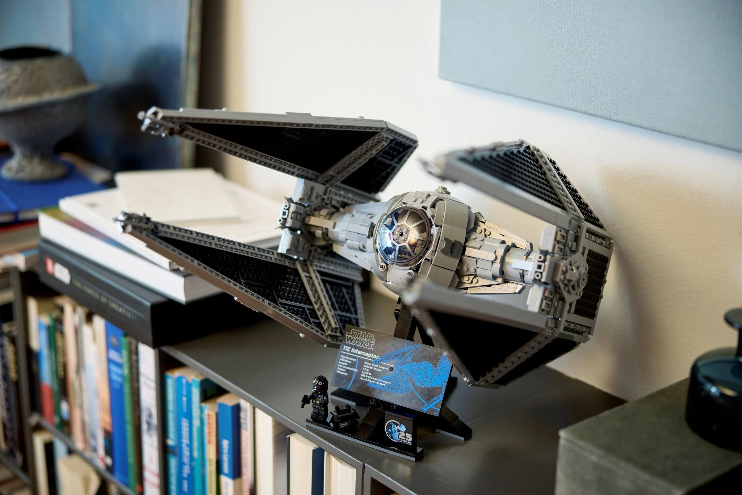 Modelul LEGO TIE Interceptor expus pe un raft, alături de o minifigură și placa informativă.