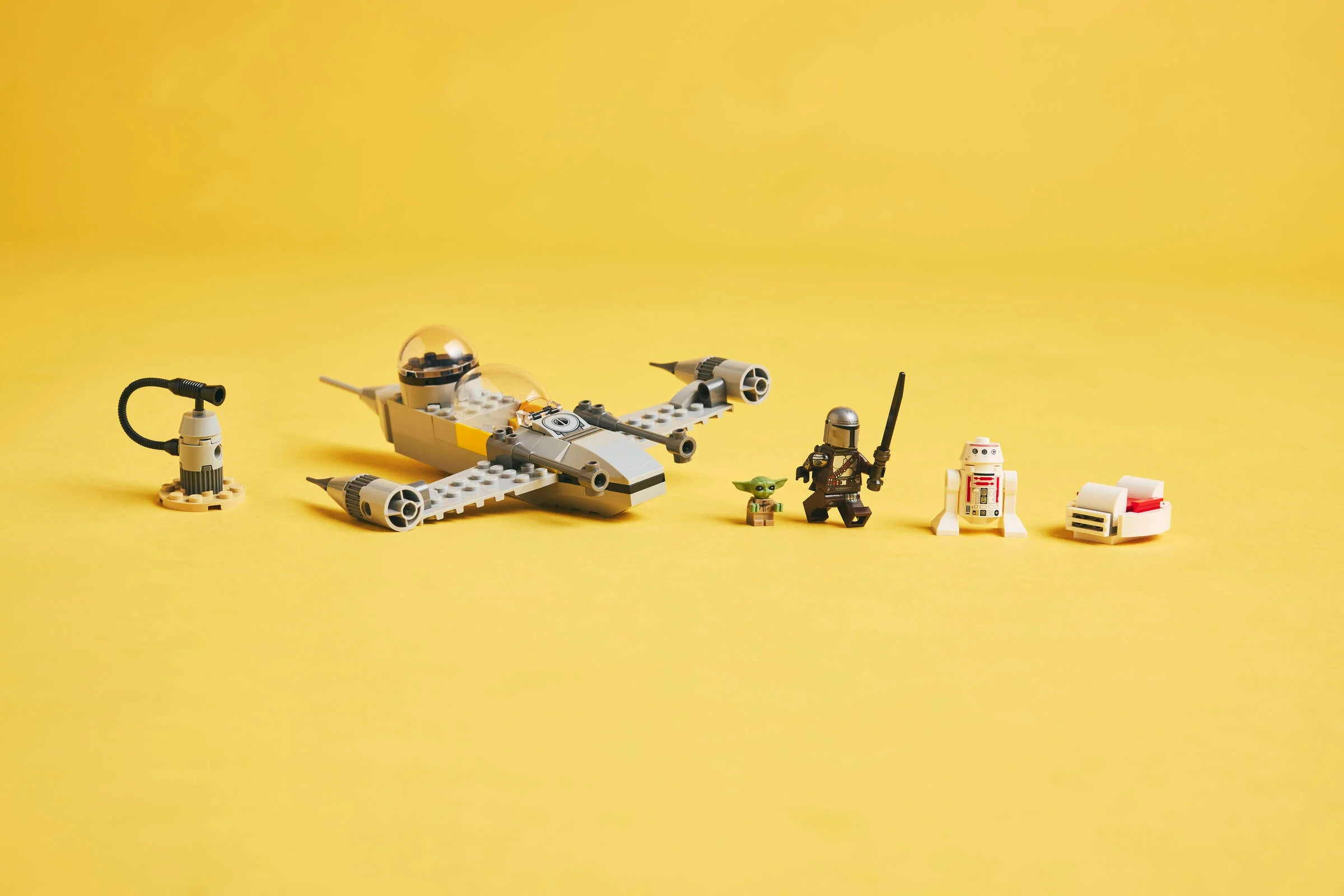 Imagine cu naveta N-1 Starfighter și minifigurinele Mando și Grogu, pe un fundal galben.
