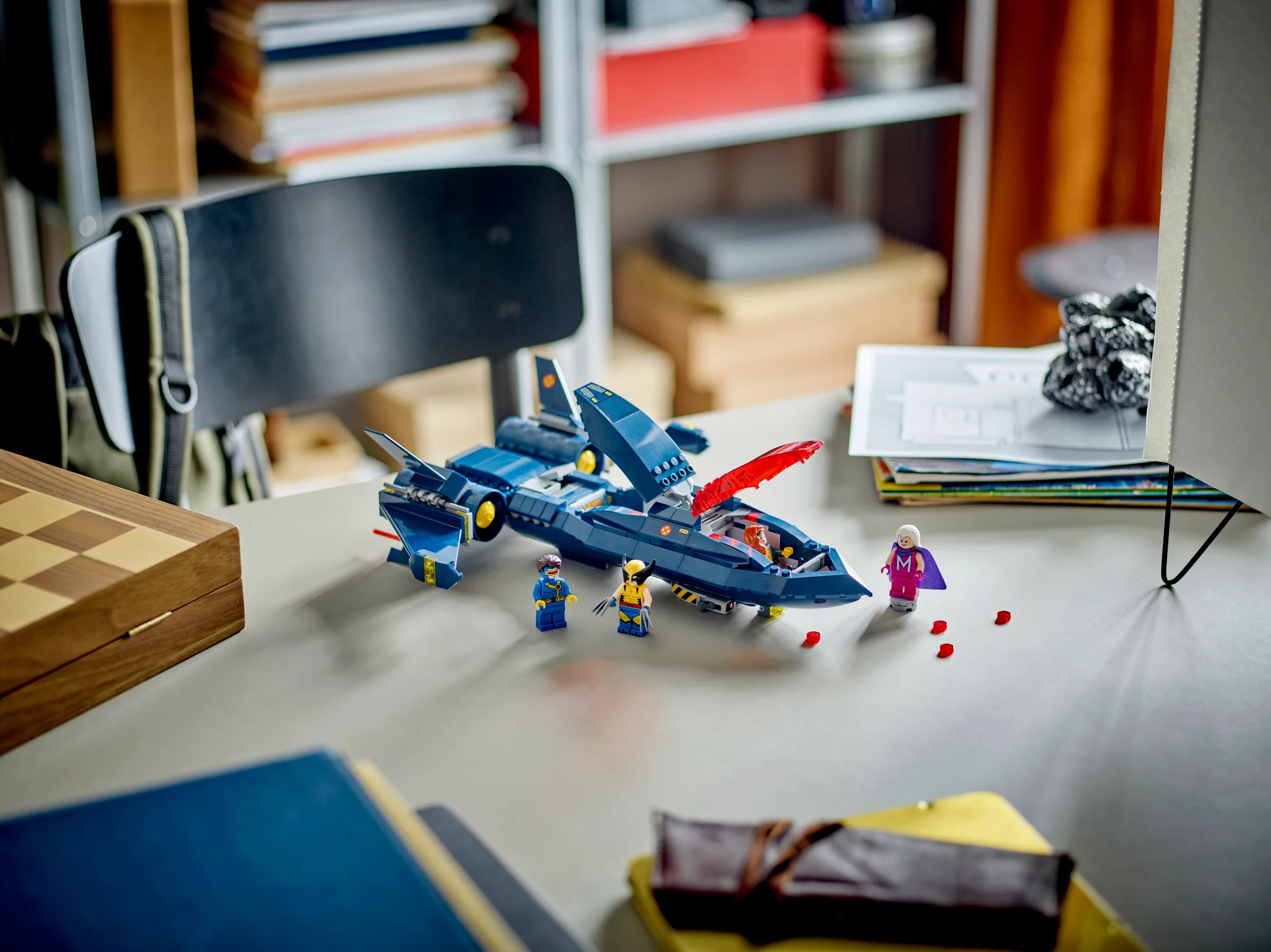X-Jet-ul X-Men 76281, cu minifigurinele Wolverine, Cyclops și Emma Frost pe o masă. Design albastru și roșu.
