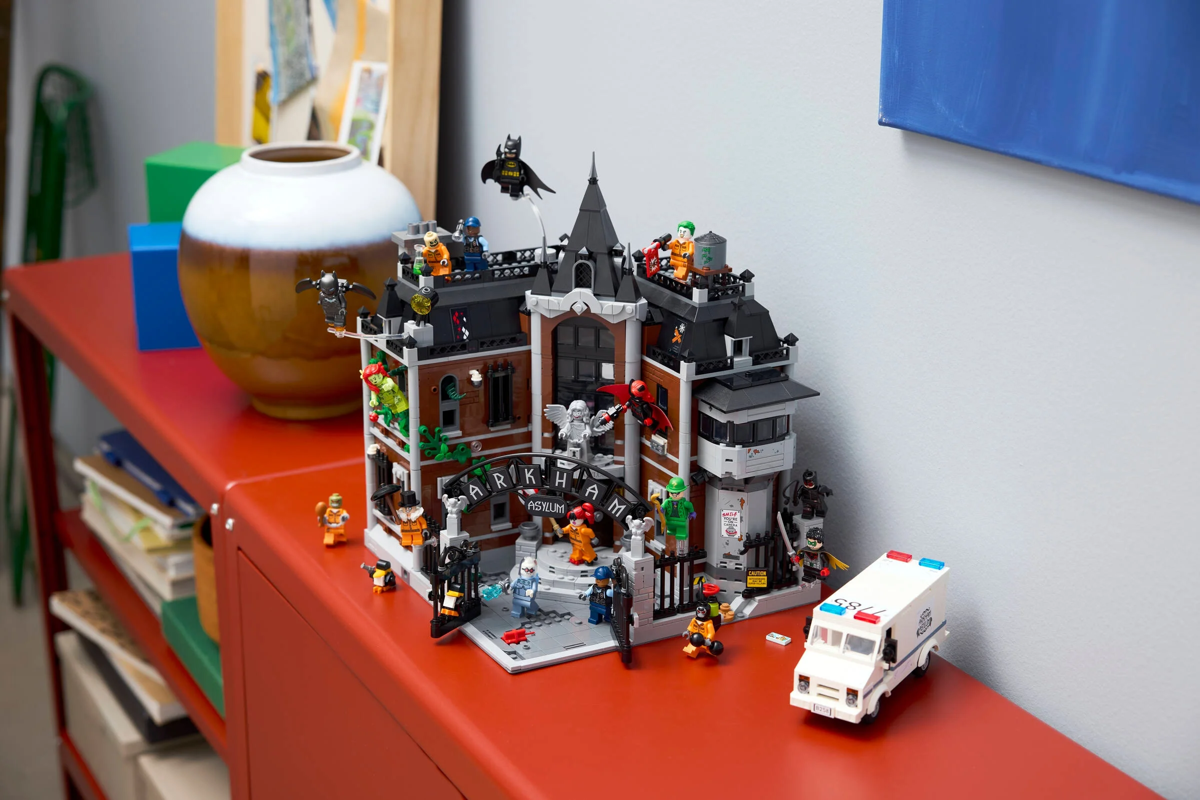 Imagine detaliată cu Arkham Asylum LEGO (76300), pe o mobilă roșie, alături de minifigurinele incluse.