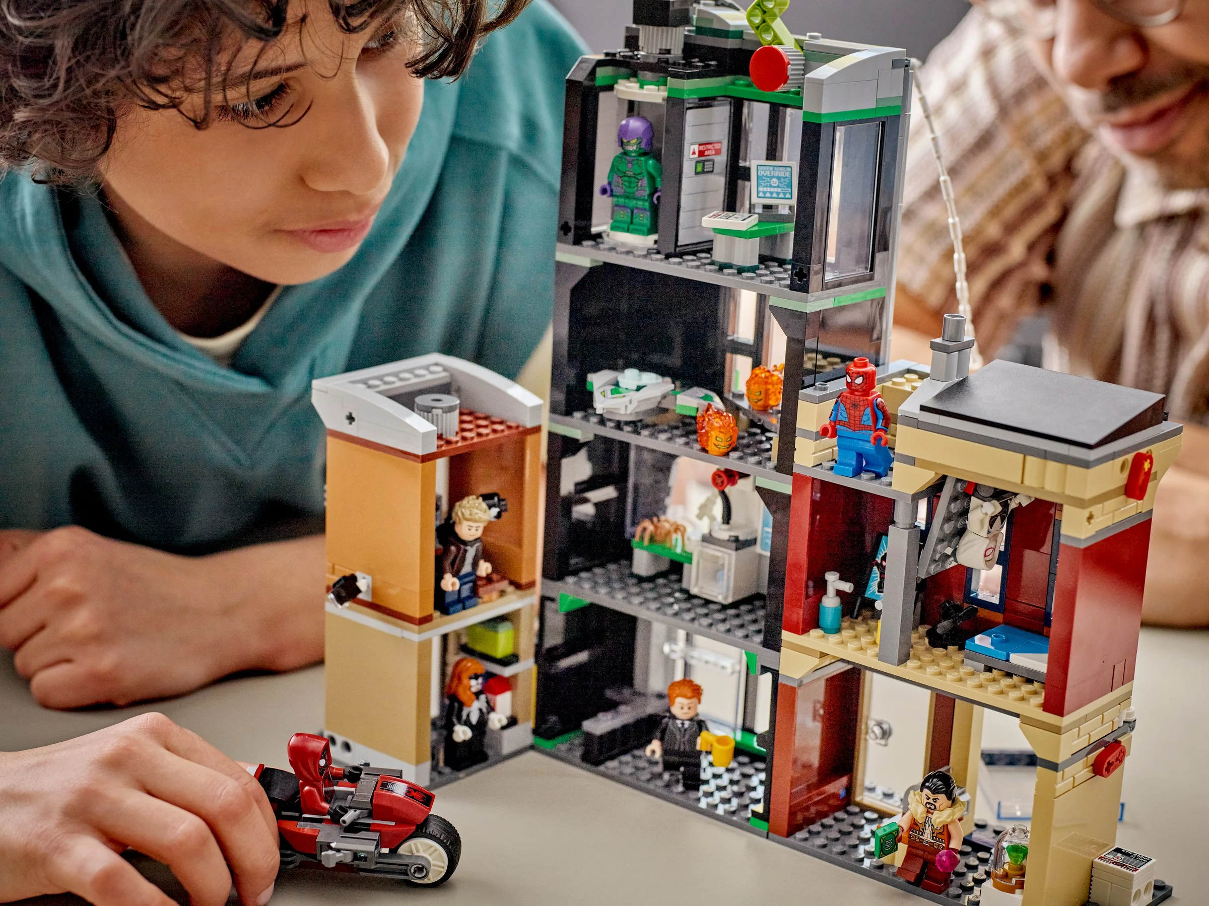 Imagine cu setul LEGO Spider-Man vs. Oscorp (76324), ce prezintă clădirile și minifigurinele. Copii interacționează.