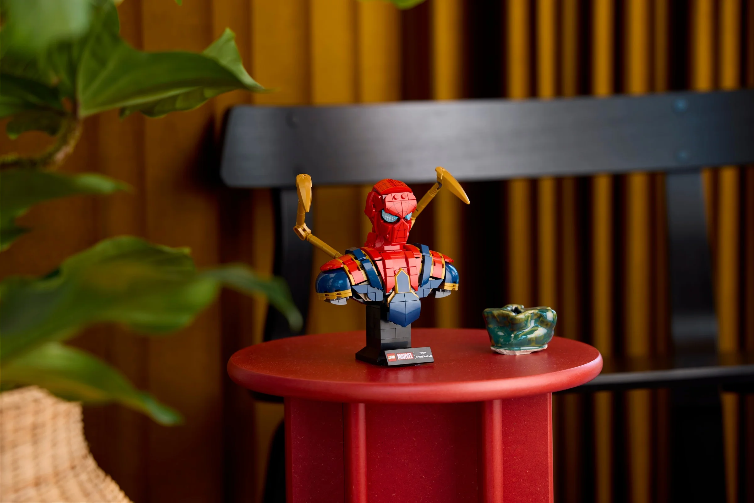 Prim-plan bustul LEGO Iron Spider-Man, pe un suport roșu, brațe aurii vizibile.
