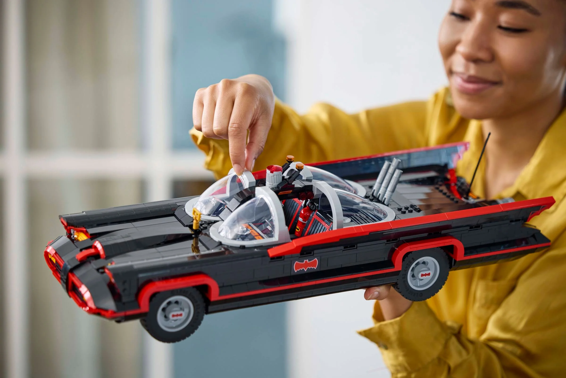 O persoană deschide cupola Batmobile-ului LEGO, model detaliat și atrăgător.