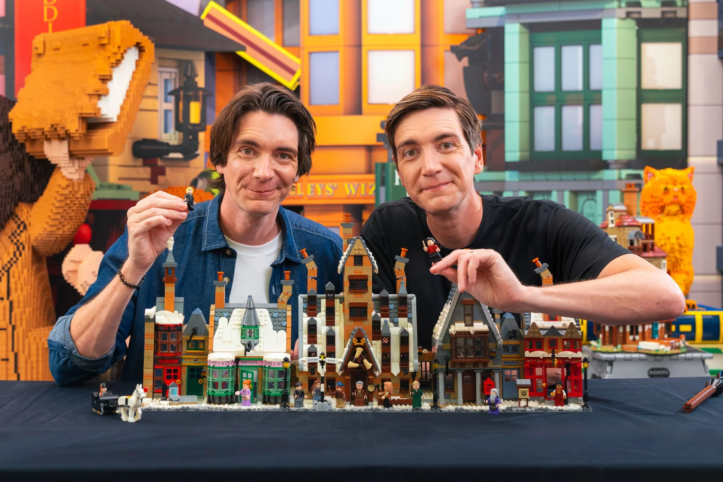 Două persoane prezintă setul LEGO Hogsmeade, o dioramă detaliată și plină de minifigurine.