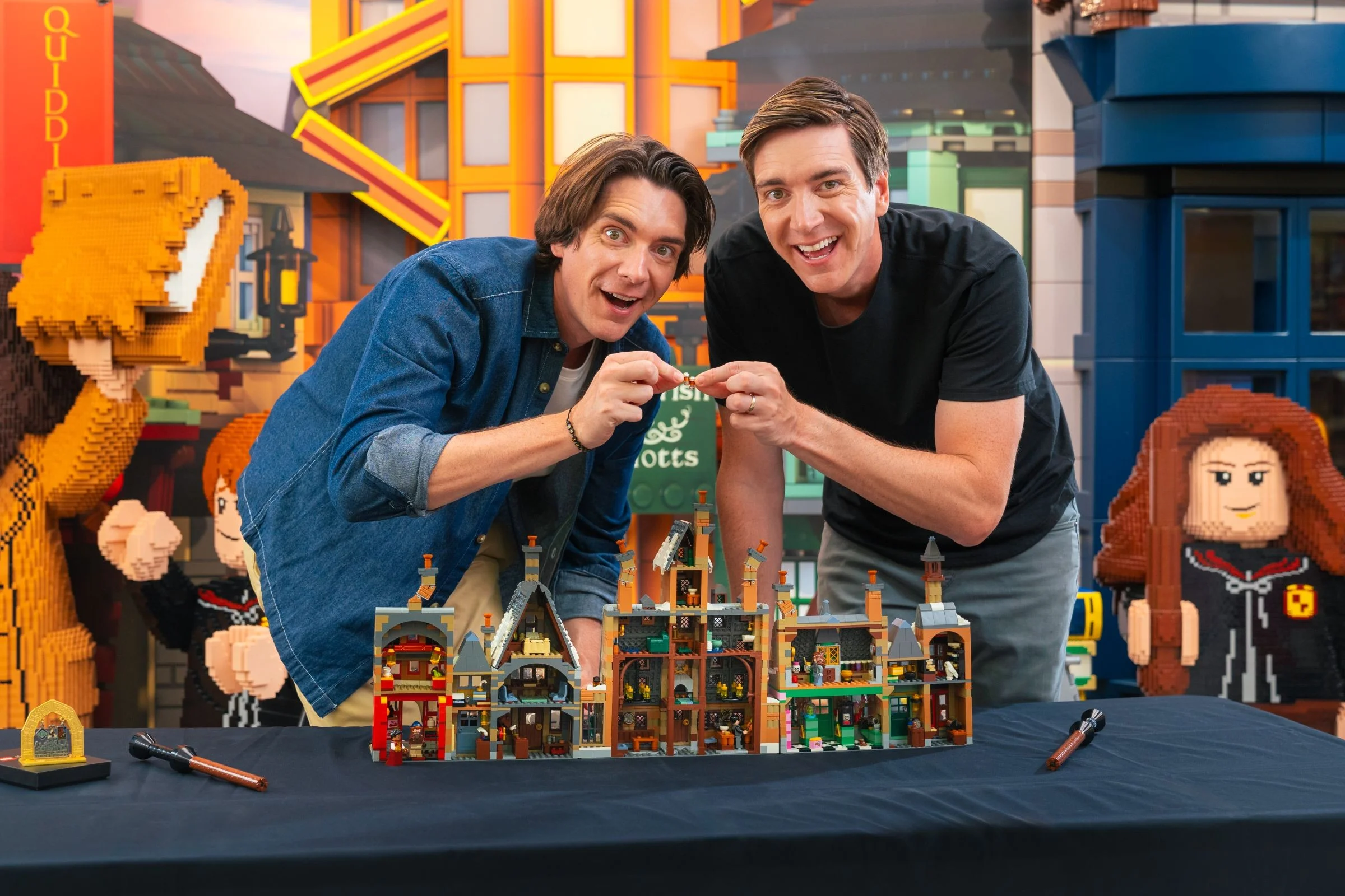 Prezentare cu doi bărbați și macheta Hogsmeade, detalii arhitecturale și minifigurine în interior.