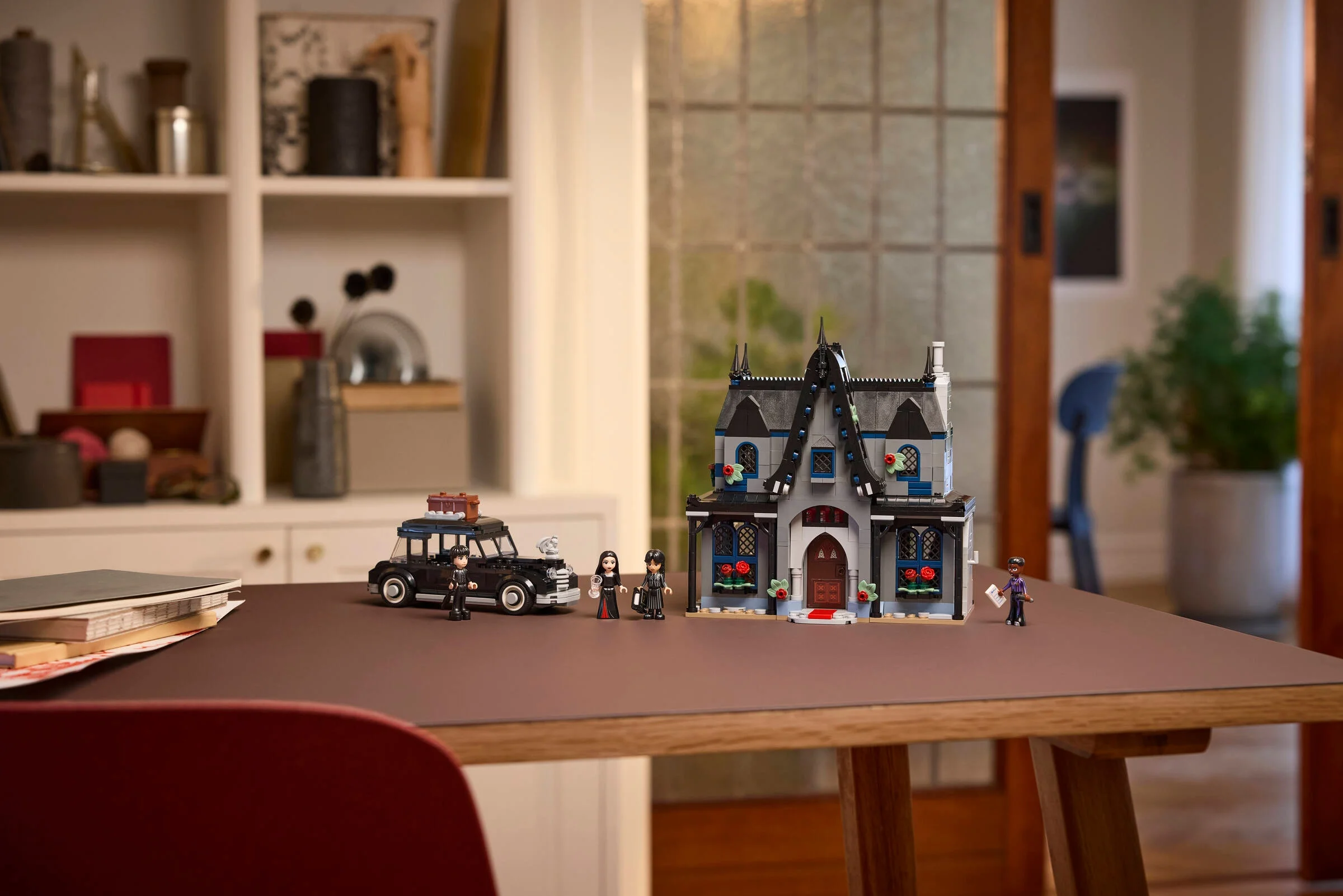 Setul LEGO 76786 Morticia's Cottage prezentat pe o masă, cu minifigurine și mașină.