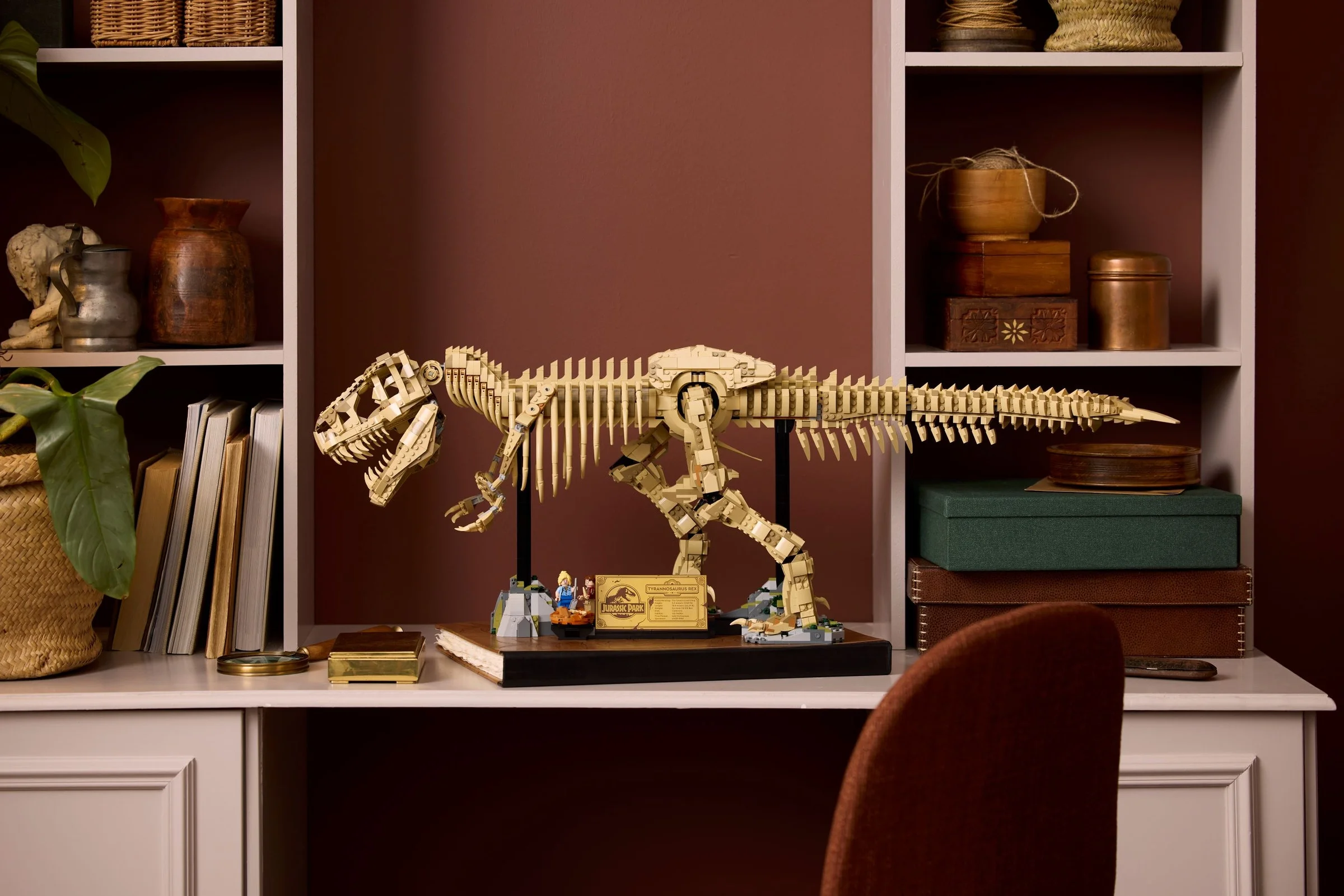 Modelul LEGO schelet de T-Rex pe un birou, alături de cărți și alte obiecte decorative.