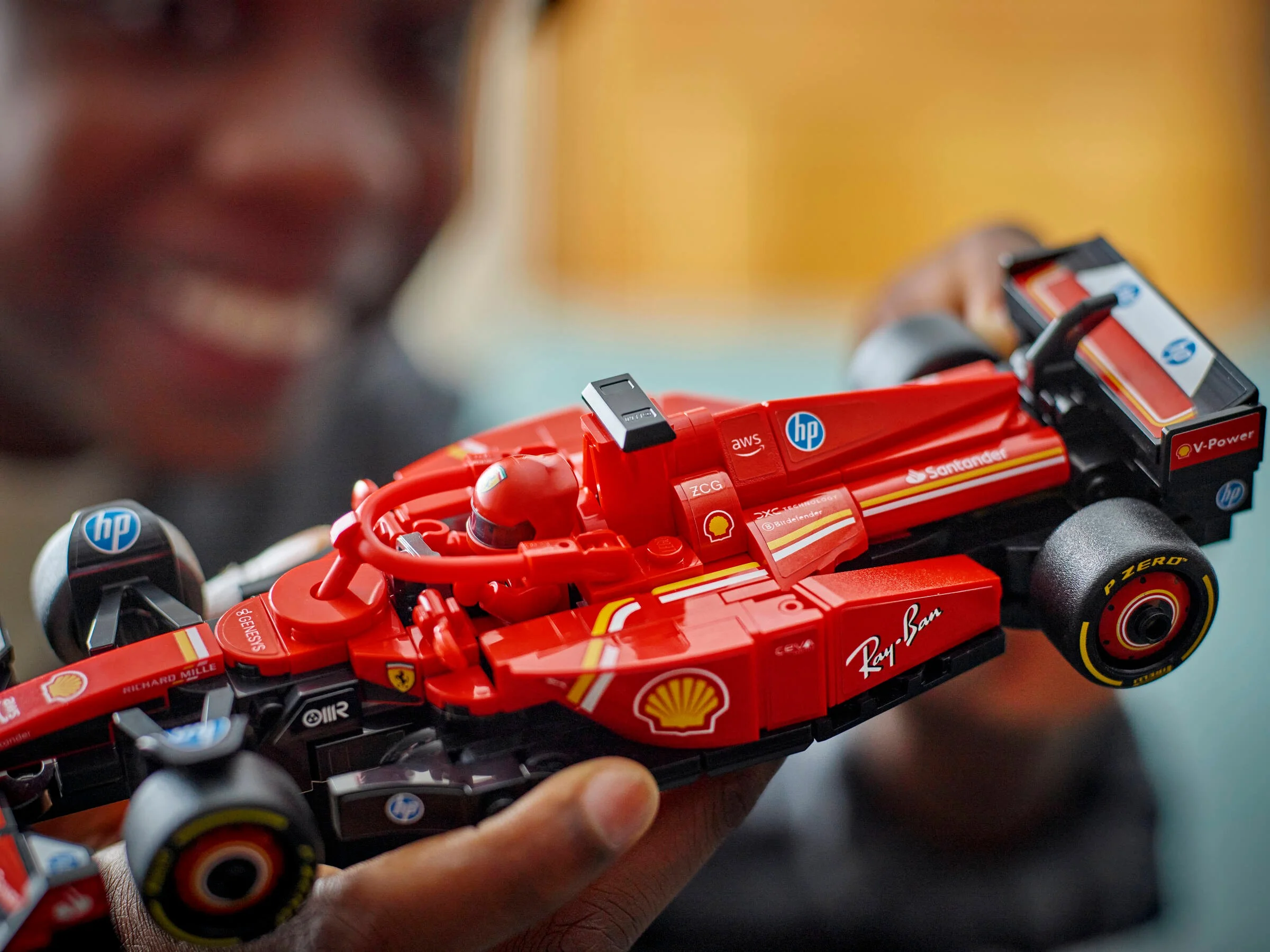 Prim-plan cu modelul LEGO Ferrari SF-24 ținut în mână, detaliind sponsorii și designul cursei.
