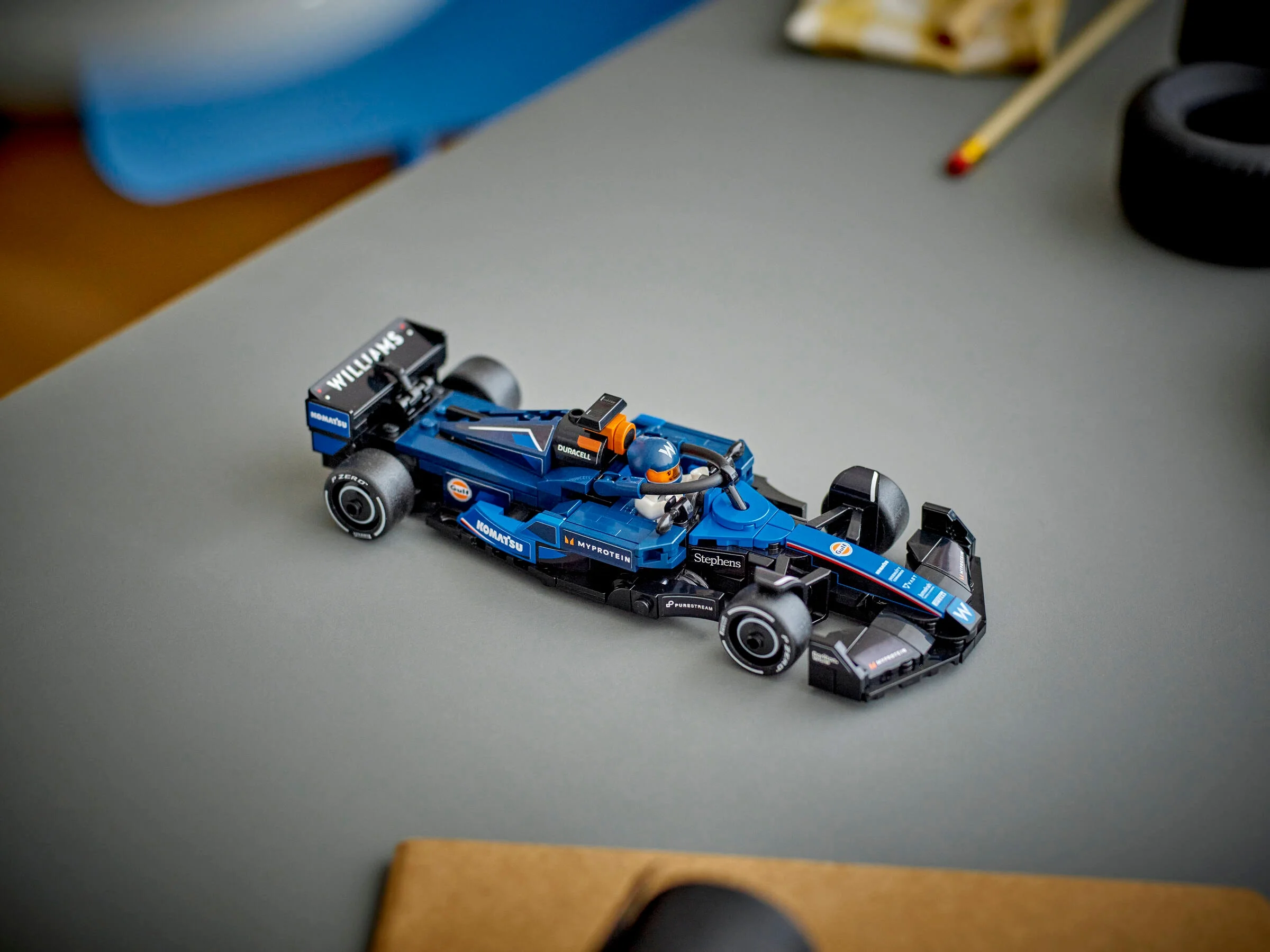 Imagine cu modelul LEGO Williams Racing FW46, o mașină albastră de curse, pe o suprafață gri.