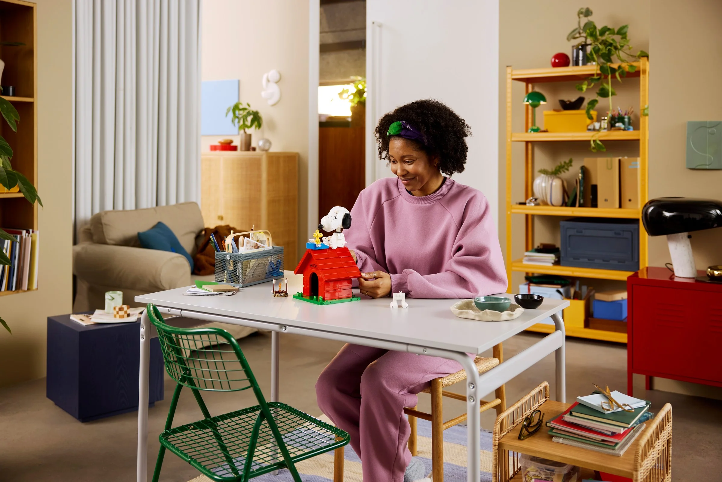 O femeie construiește căsuța lui Snoopy din LEGO, într-o atmosferă relaxată, de interior.