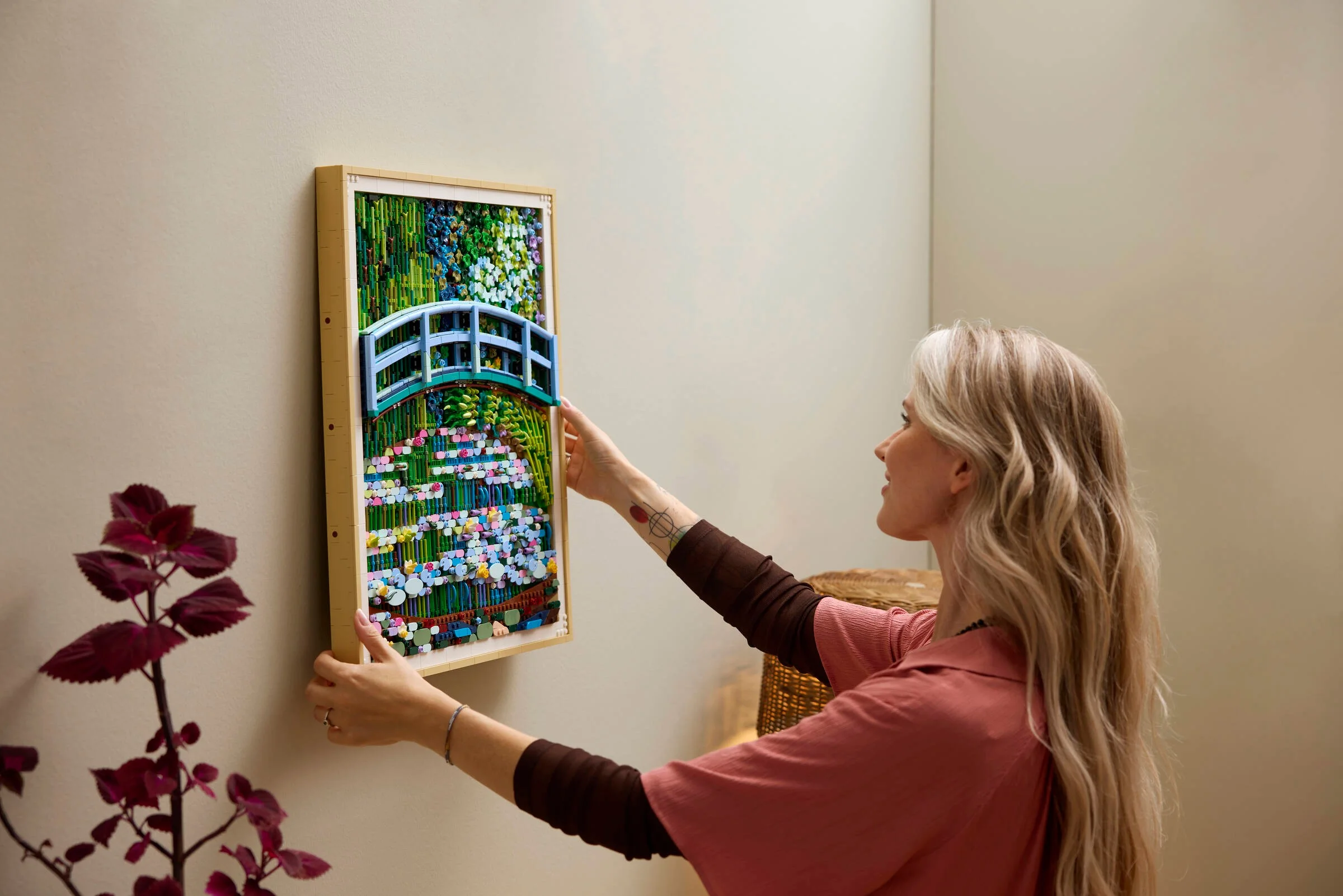 O femeie montează tabloul LEGO Monet pe perete, într-o cameră luminoasă.
