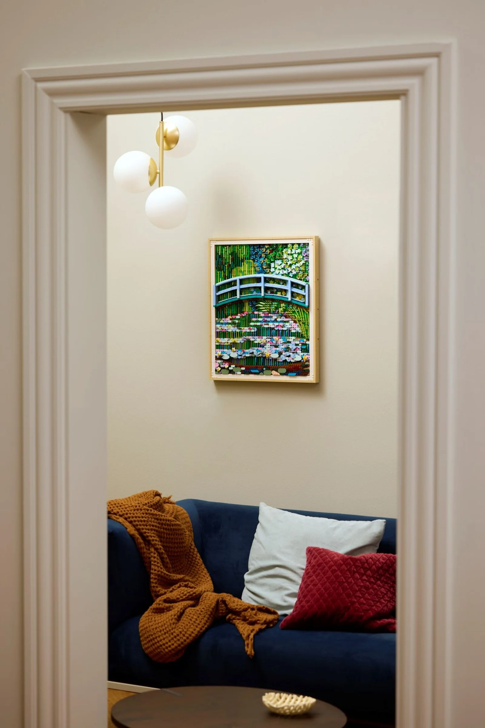 Tabloul LEGO Monet pe perete, văzut printr-o ușă, decorând un living cochet.