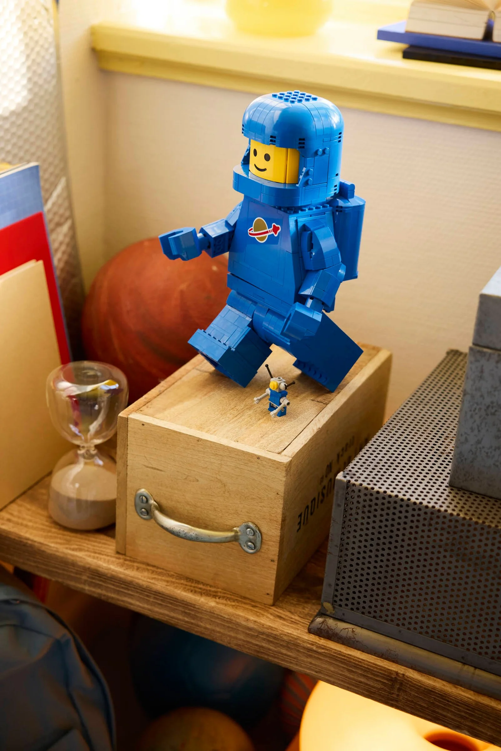 Astronautul albastru LEGO pe o cutie de lemn, într-un decor casnic. Imaginea este clară și detaliată.
