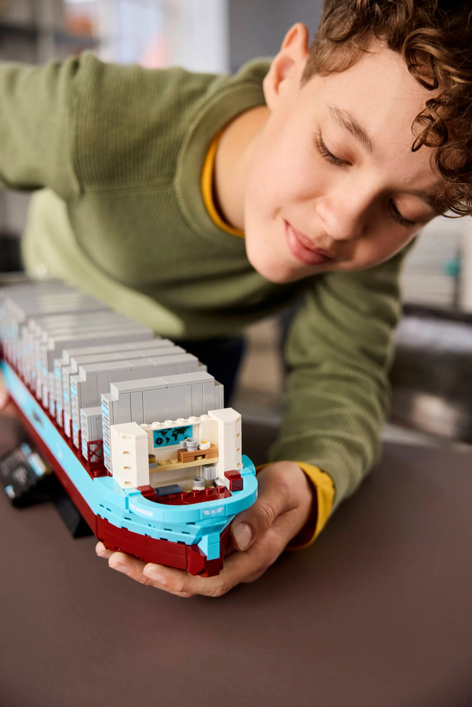 Băiat admirând nava container Maersk, cu detalii interioare vizibile, în mâinile sale.