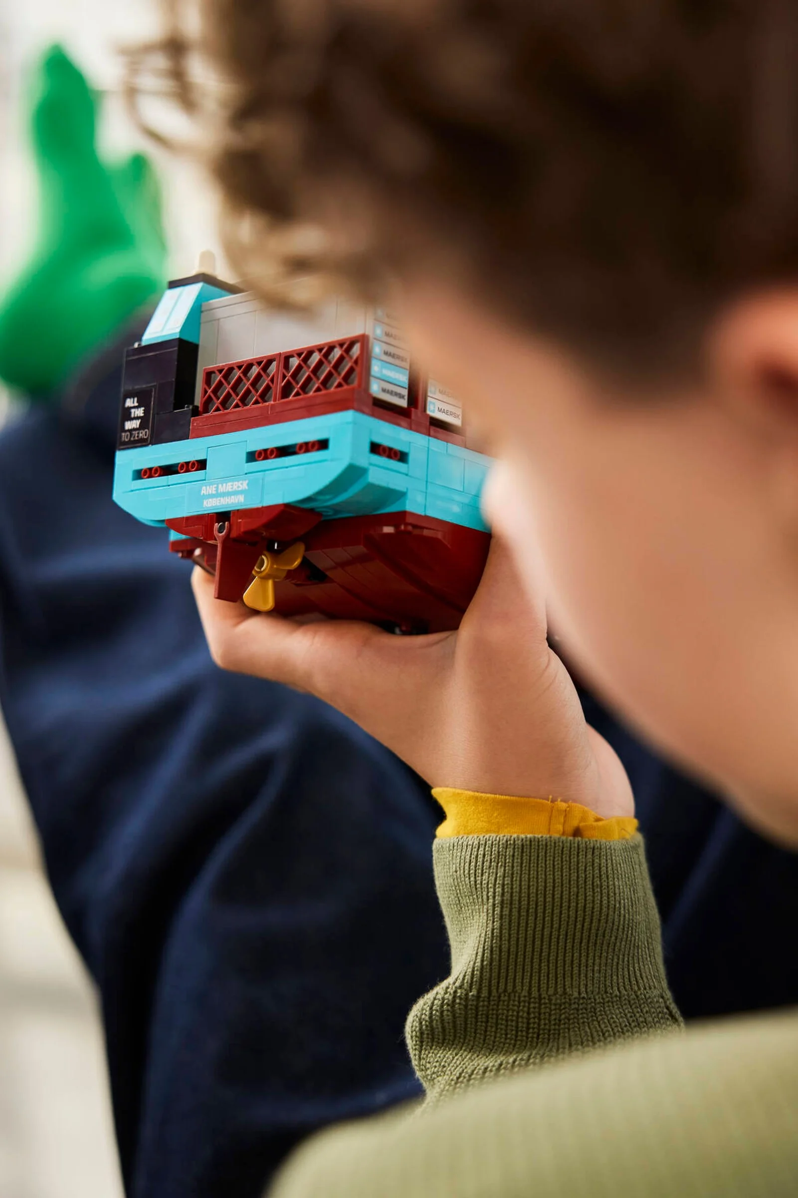 Un băiat ține în mână modelul LEGO al navei Maersk, admirându-l de aproape.