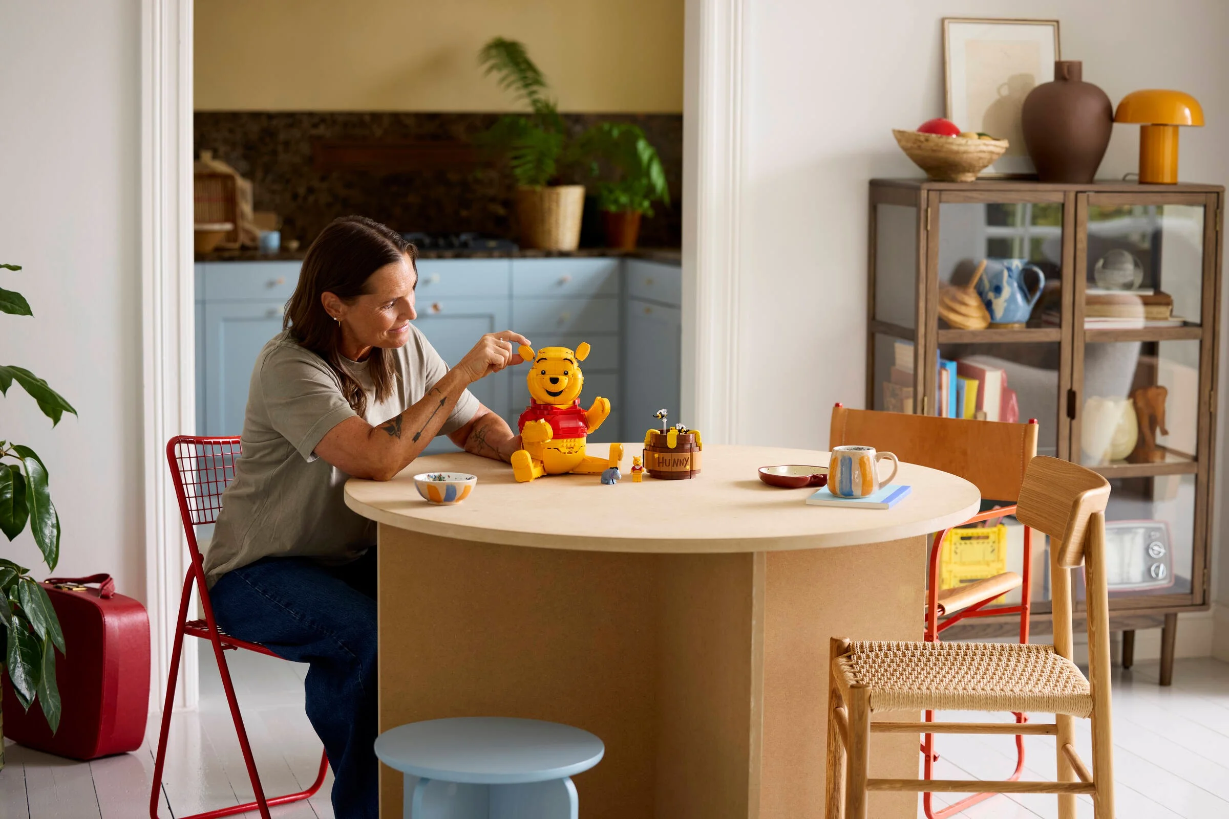O femeie interacționează cu modelul LEGO Winnie the Pooh la o masă.