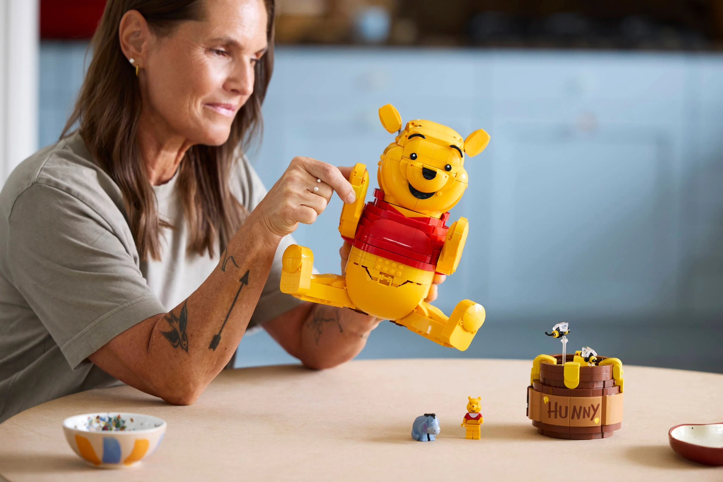 O femeie ține în mână modelul Lego Winnie the Pooh, zâmbind.