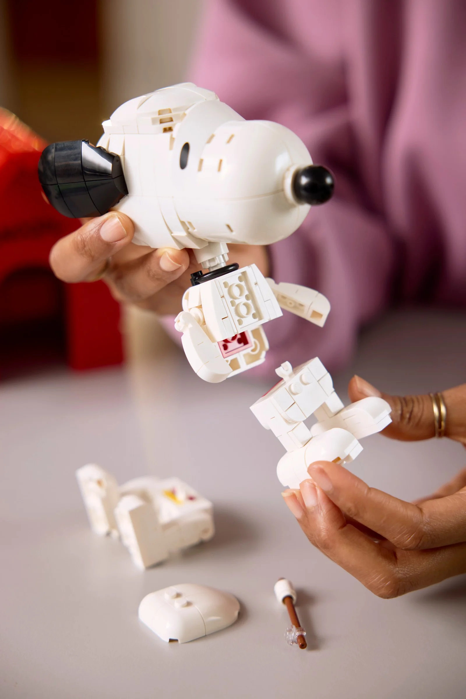 Construirea lui Snoopy: mâini asamblând figurina LEGO Snoopy. Detalii de construcție vizibile.