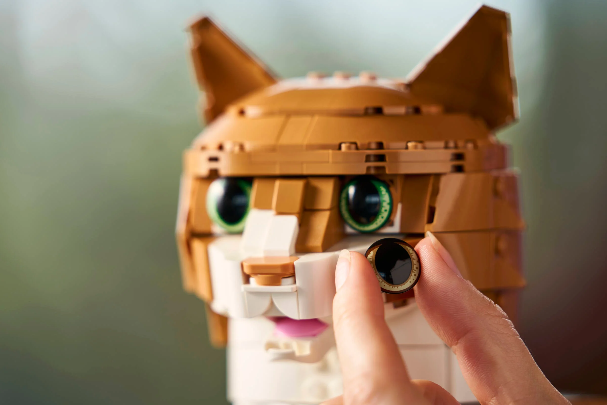 Prim-plan cu pisica portocalie LEGO 21376, punând un ochi detașabil. Detaliu construcție complexă.