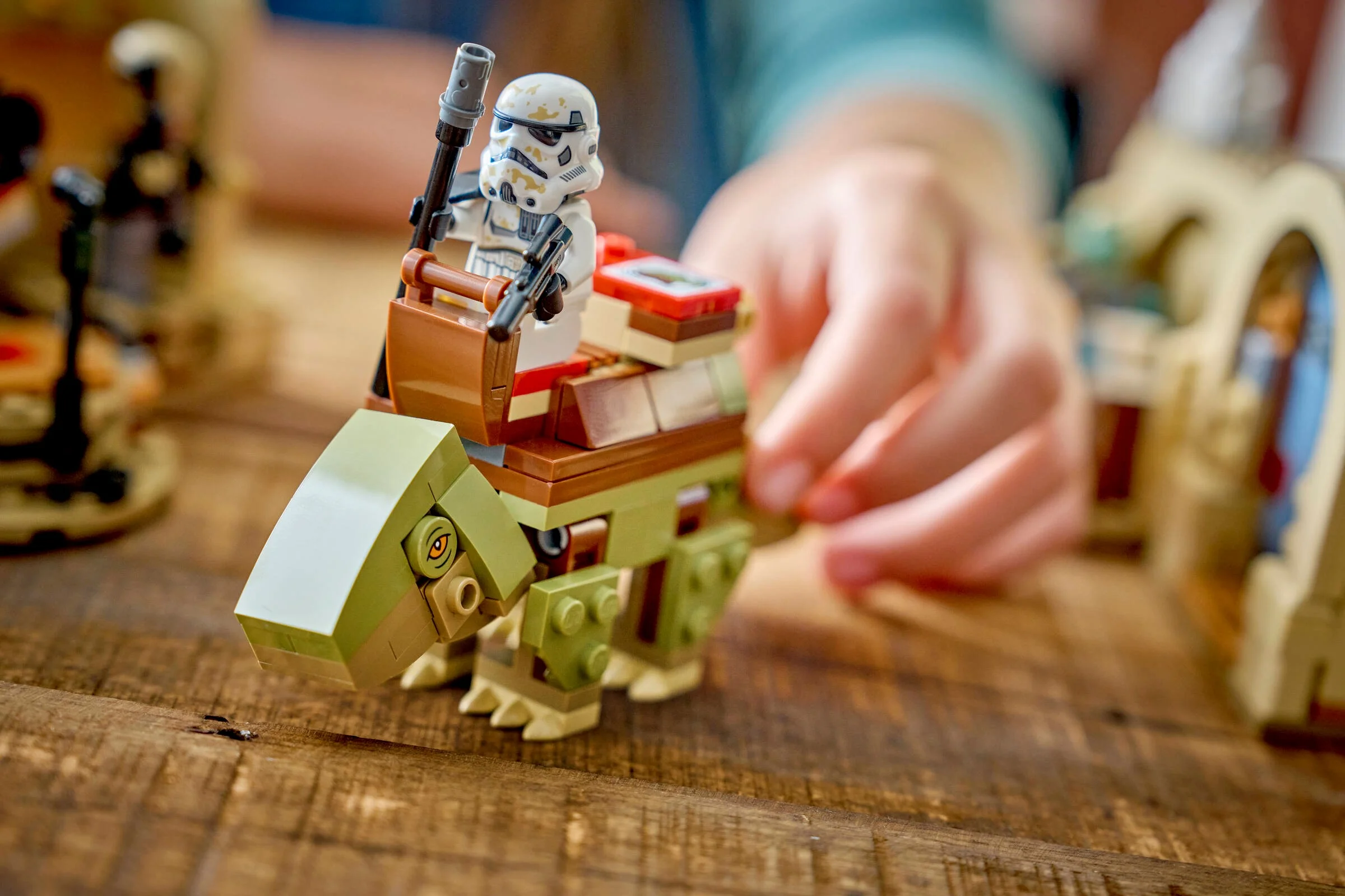 Figurină Stormtrooper pe un Dewback LEGO. O mână apare în fundal. Detaliu al setului Mos Eisley.