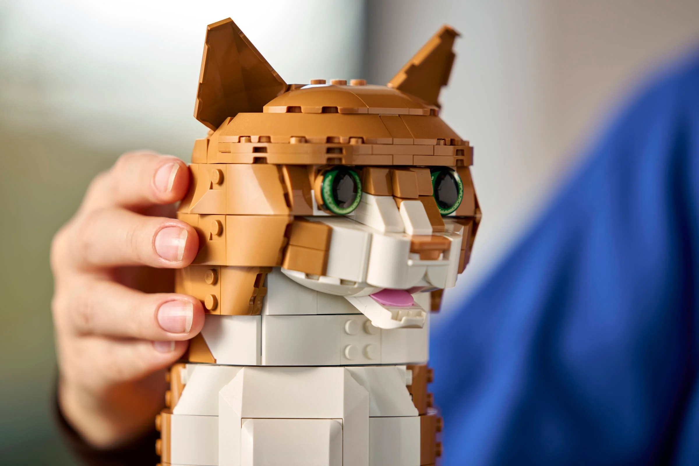 Prim-plan cu pisica portocalie LEGO, asamblată și ținută de o persoană. Detalii realiste ale ochilor și blănii.