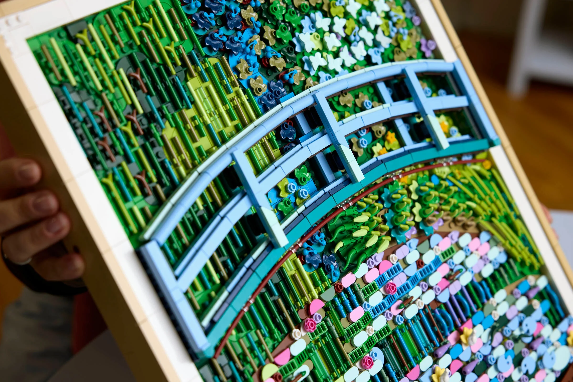 Imagine detaliată a modelului LEGO Monet, cu podul și nuferii, într-un cadru din lemn.