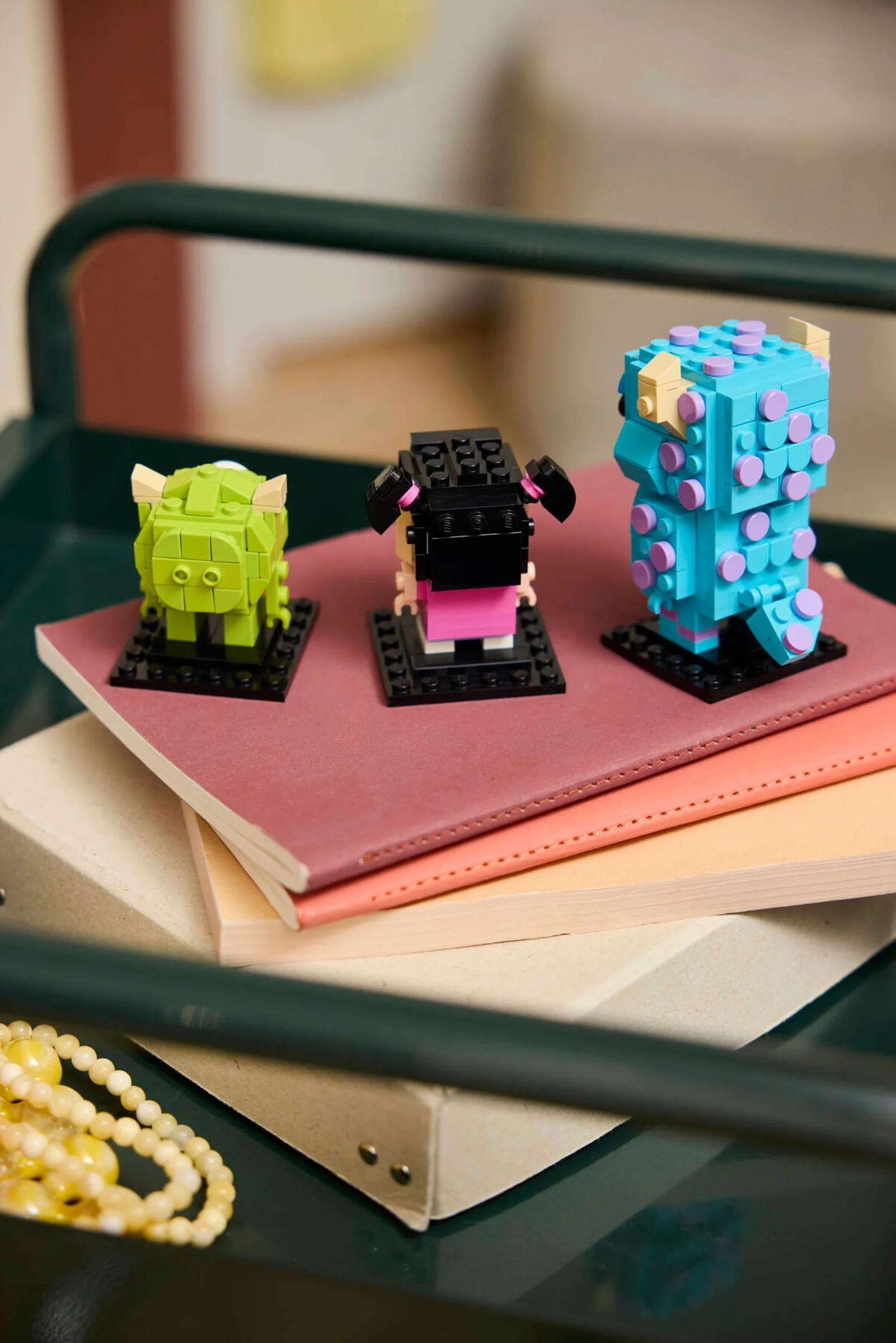 Figurinele BrickHeadz Sulley, Mike și Boo, așezate pe o stivă de caiete. O prezentare drăguță și colorată.