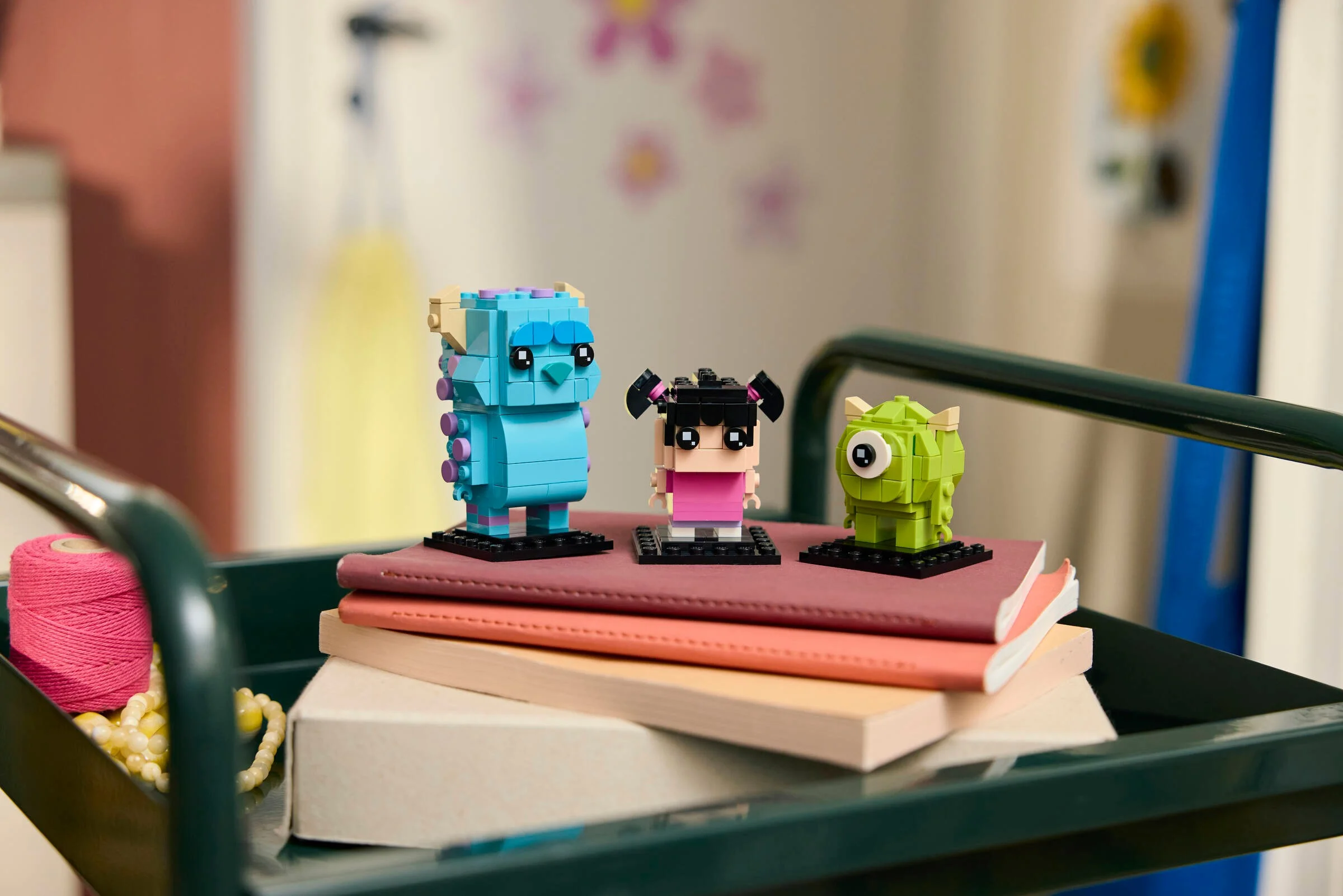 Imagine cu figurinele Sulley, Mike și Boo din setul BrickHeadz 40861, aranjate pe o căruță.