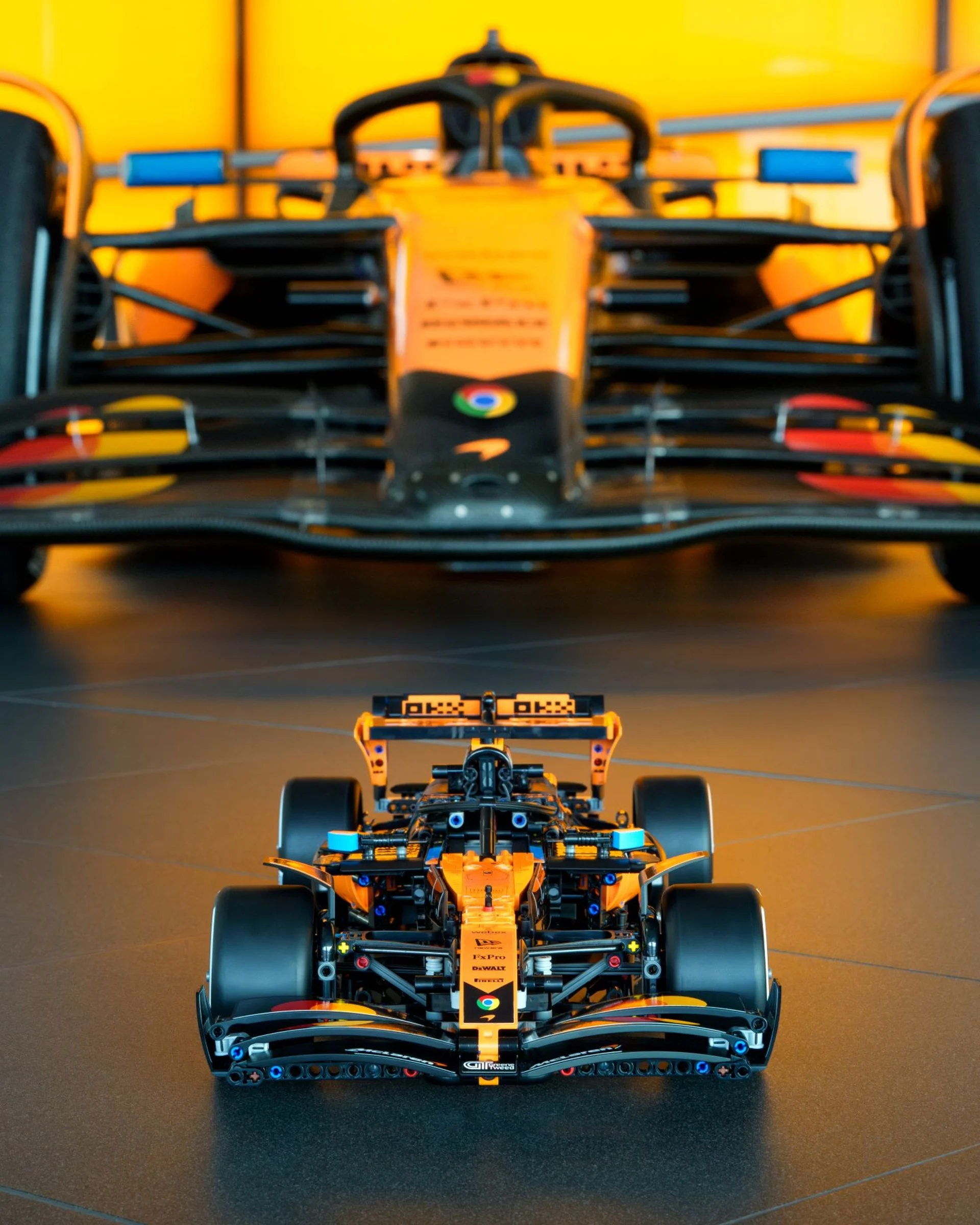 Imagine frontală cu modelul LEGO McLaren F1 Team MCL39 și mașina reală în fundal.